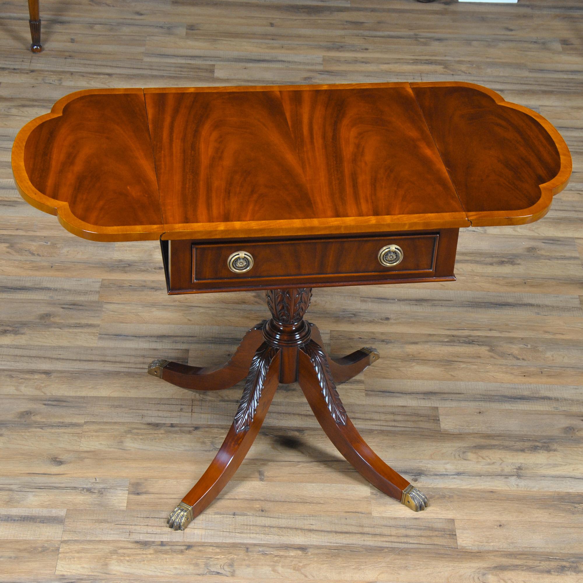 A large Duncan Phyfe style Dropside Table from Niagara Furniture with a beautifully crafted top featuring figural mahogany and satinwood, a dovetailed drawer and two fold down dropside leaves supported by solid mahogany arms when opened. The base of