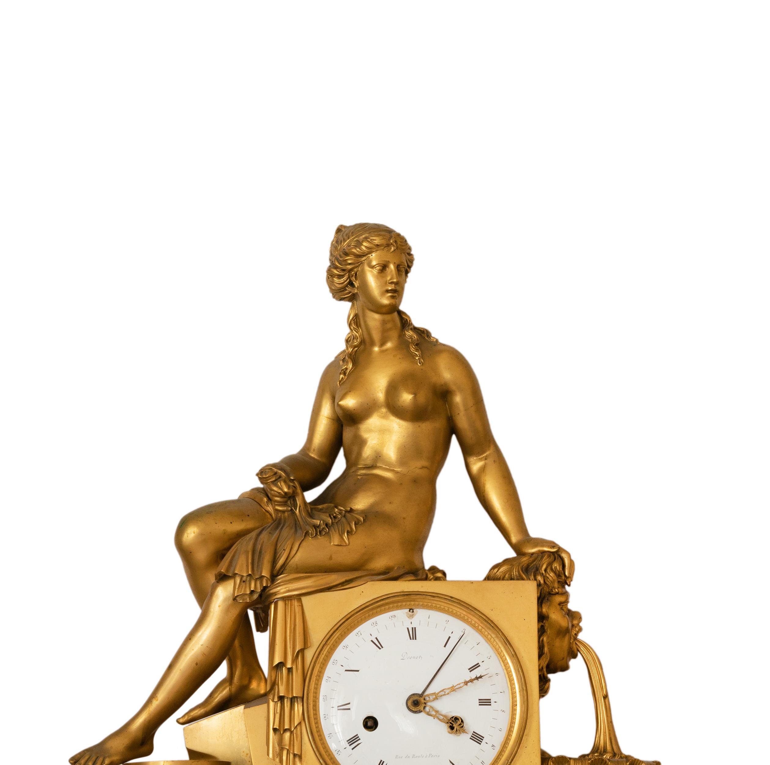 This French Empire mantel clock features a seated female figure, finely sculpted, draped in flowing fabric, and positioned next to an elegant water fountain motif.
The round enamel dial is centrally placed, adorned with Roman numerals and delicate