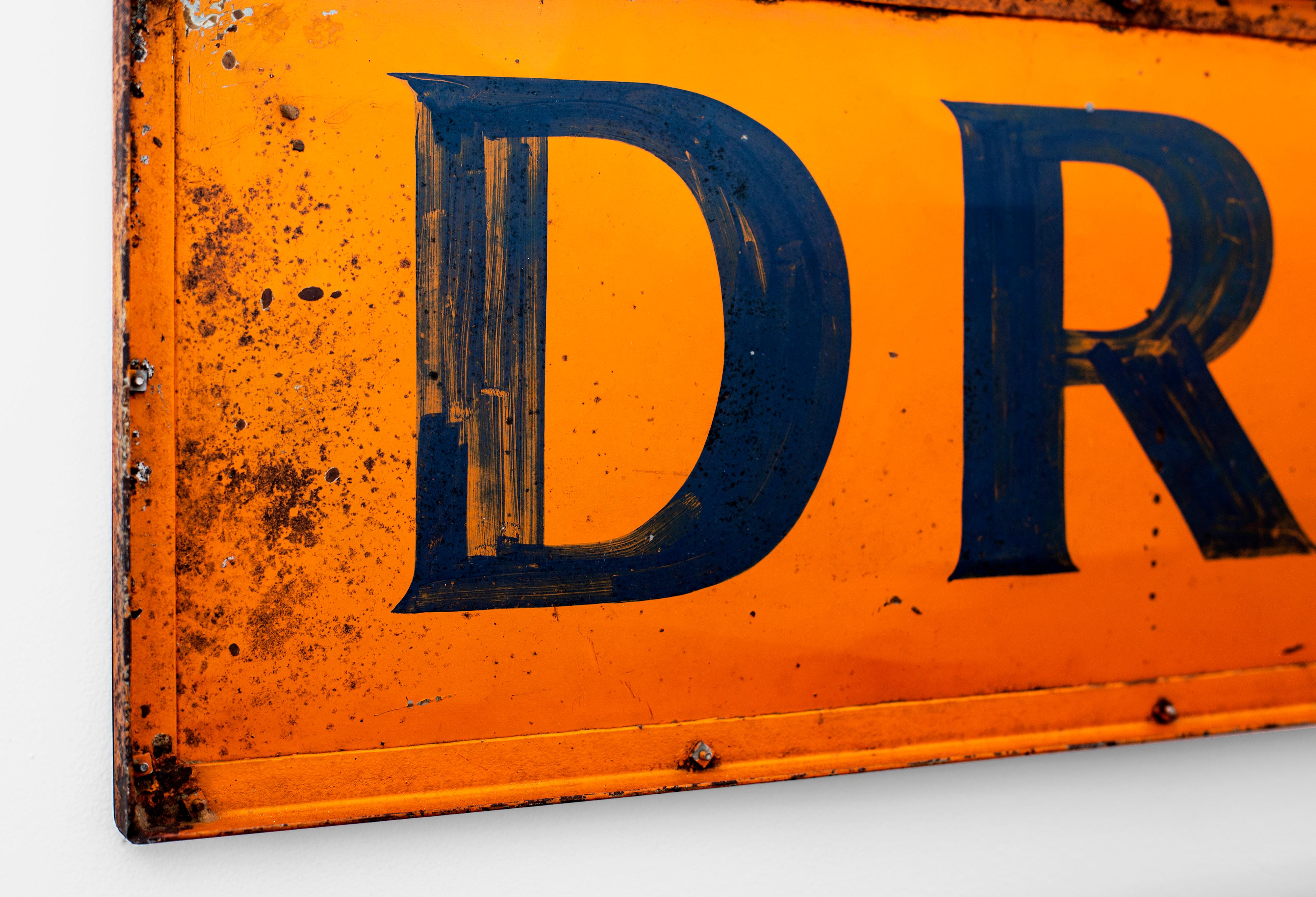Large metal sign that reads DRUGS. Original orange and blue paint has great age and patina. Chips, scratches and rust add to the character of the piece.