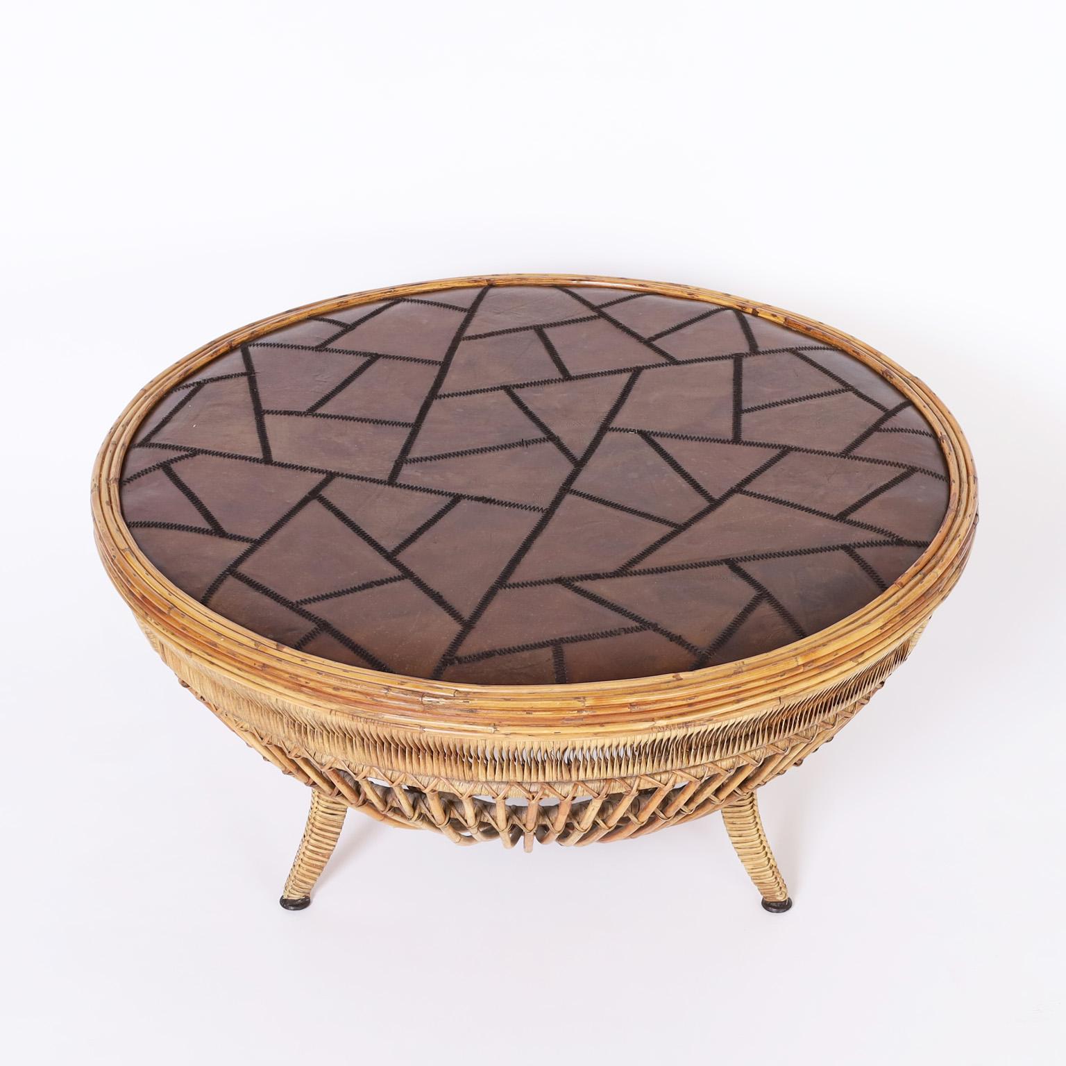 Table basse de style colonial britannique avec un plateau rond composé d'une mosaïque abstraite de cuir cousu sur une forme de tambour classique réalisée en rotin enrobé de roseau sur trois pieds enveloppés.