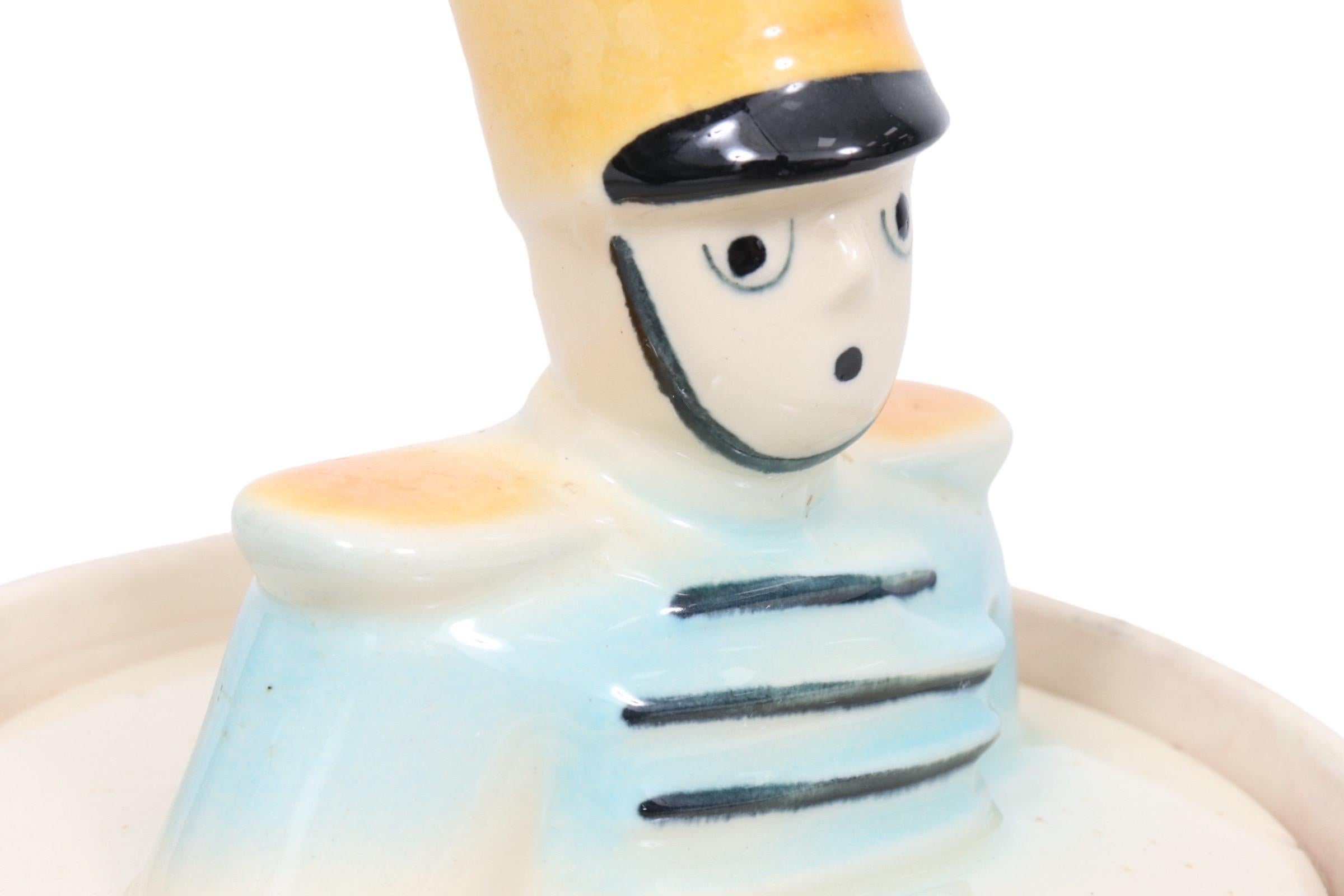 A collectible ceramic cookie jar shaped like a drum, trimmed in red and decorated with a drummer boy in yellow and blue. The lid lifts off with a matching drummer bust. Designed by Robert Heckman for Shawnee Pottery. Marked USA 10 underneath.