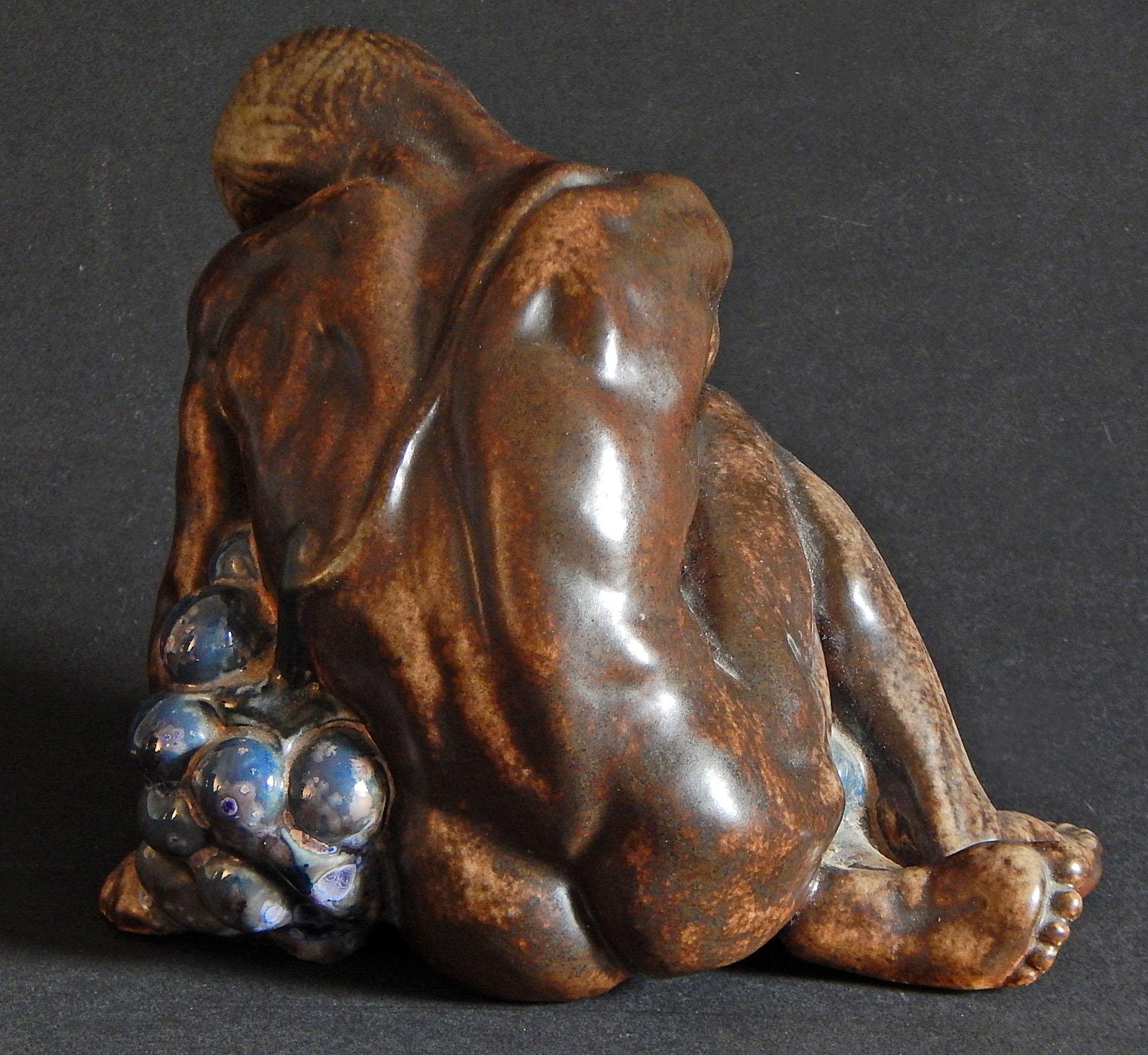 This sensuous ceramic piece depicts a beautifully sculpted nude figure embracing an exaggerated grape cluster, sculpted by Kai Nielsen for Bing & Grondahl in Copenhagen. While all examples of this piece are rare, the glazes here are extremely
