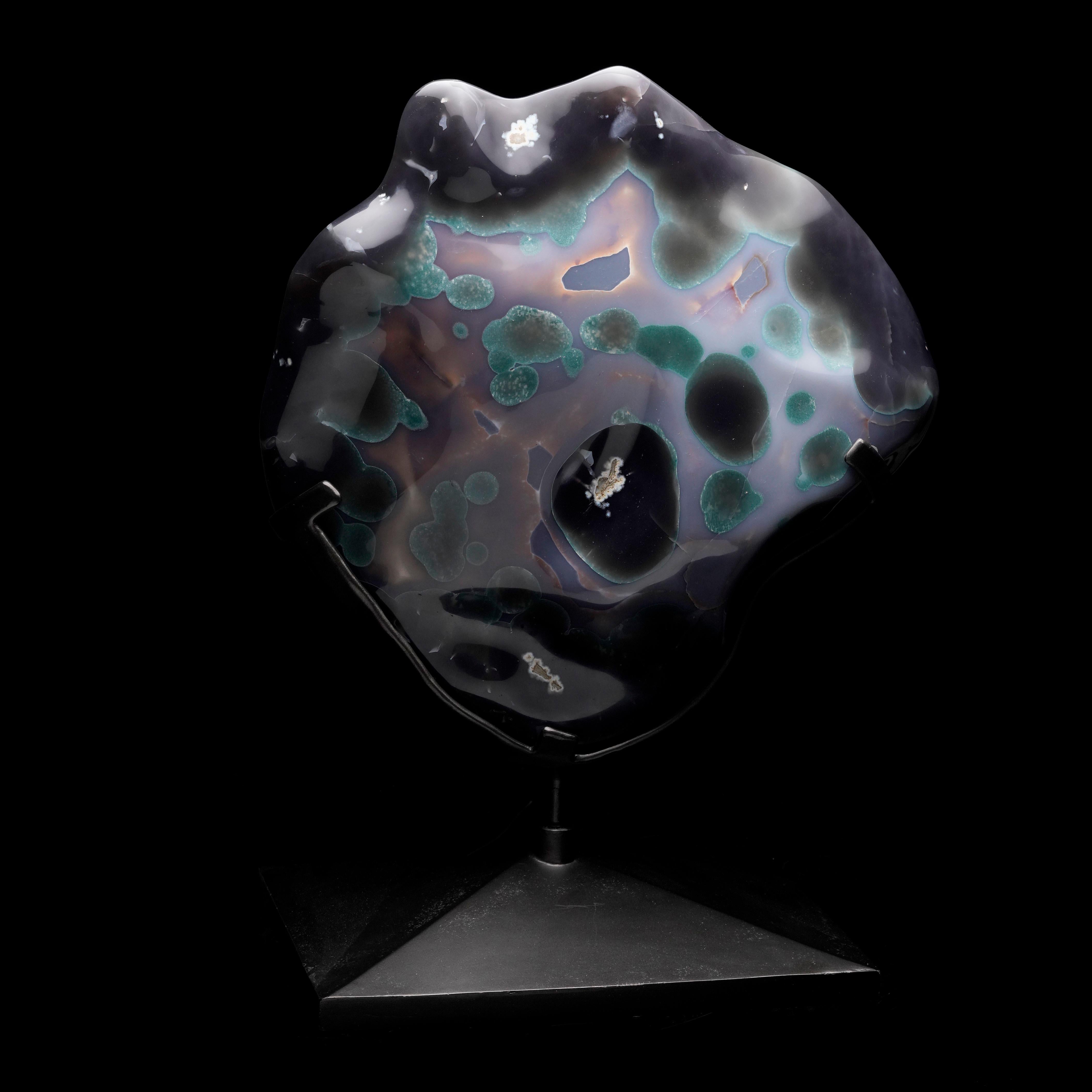 This striking specimen is a slice of Uruguayan agate hand-polished around the sides and over the stunning back and mounted on a sleek, custom black metal base that rotates 360 degrees. The agate displays bands of gray, blue, and white tones