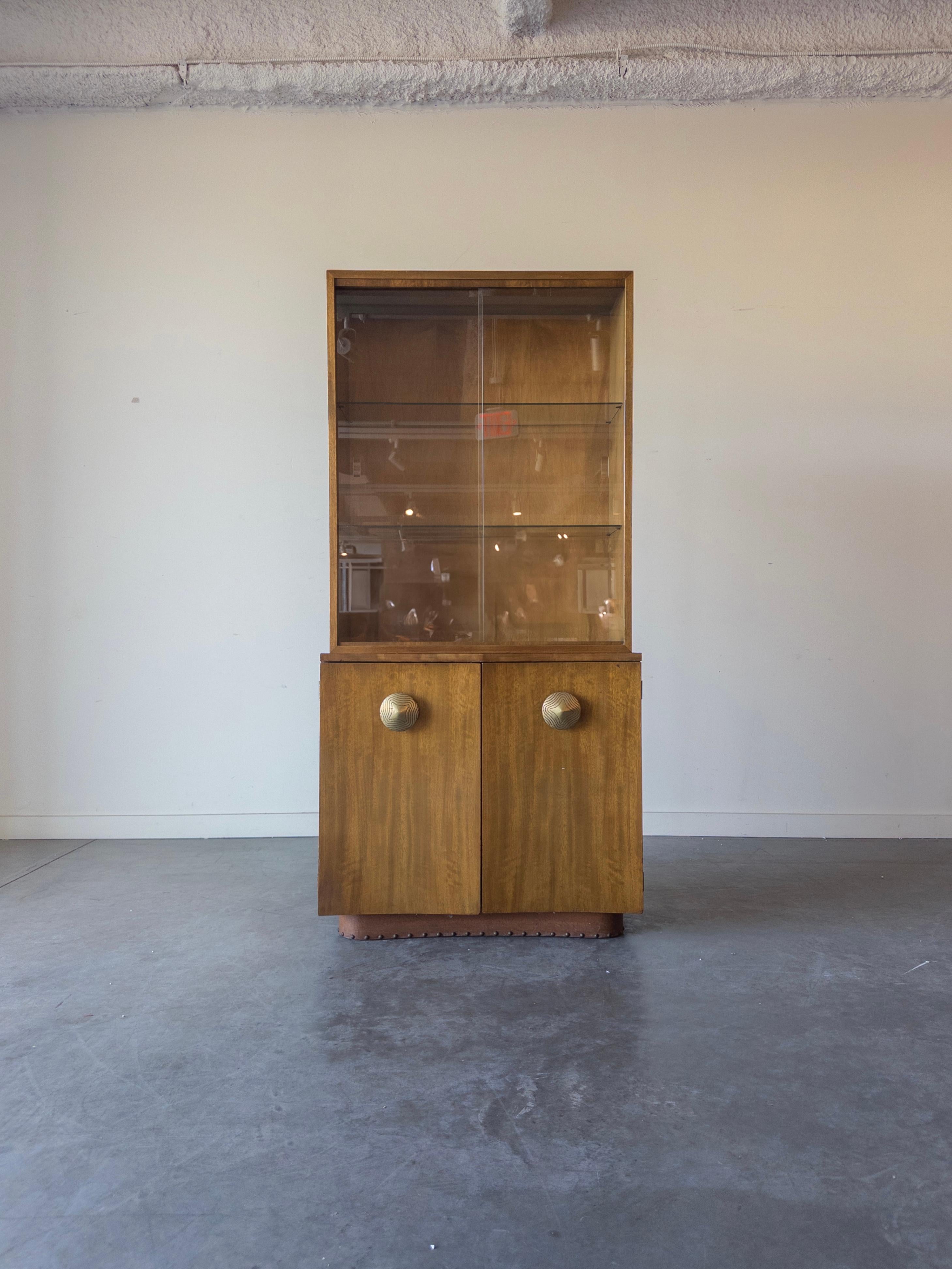 Der Gilbert Rohde Gruppenschrank Nr. 4190 Paldao verfügt über zwei Glasschiebetüren, hinter denen sich zwei verstellbare Glasböden verbergen, und zwei Türen, hinter denen sich ein fester Boden verbirgt. Etikett des Papierherstellers auf der