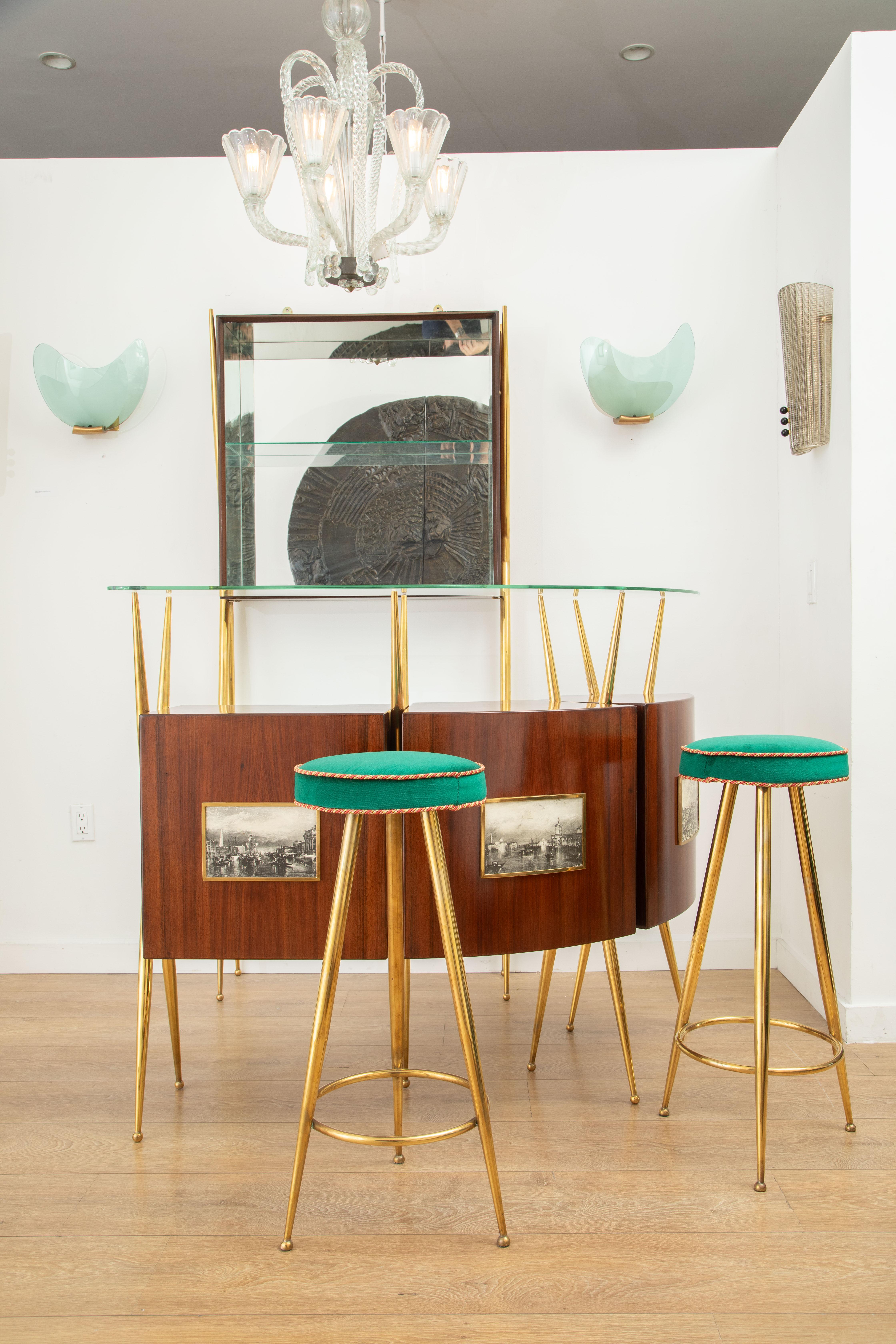 Dry bar suite, in the style of Gio Ponti, Italy 1950
An exceptional dark cherry wood veneer and brass 1950's Italian bar suite comprised of:
 A curved dry bar with glass top and lots of storage compartments
 Two brass stools newly upholstered with