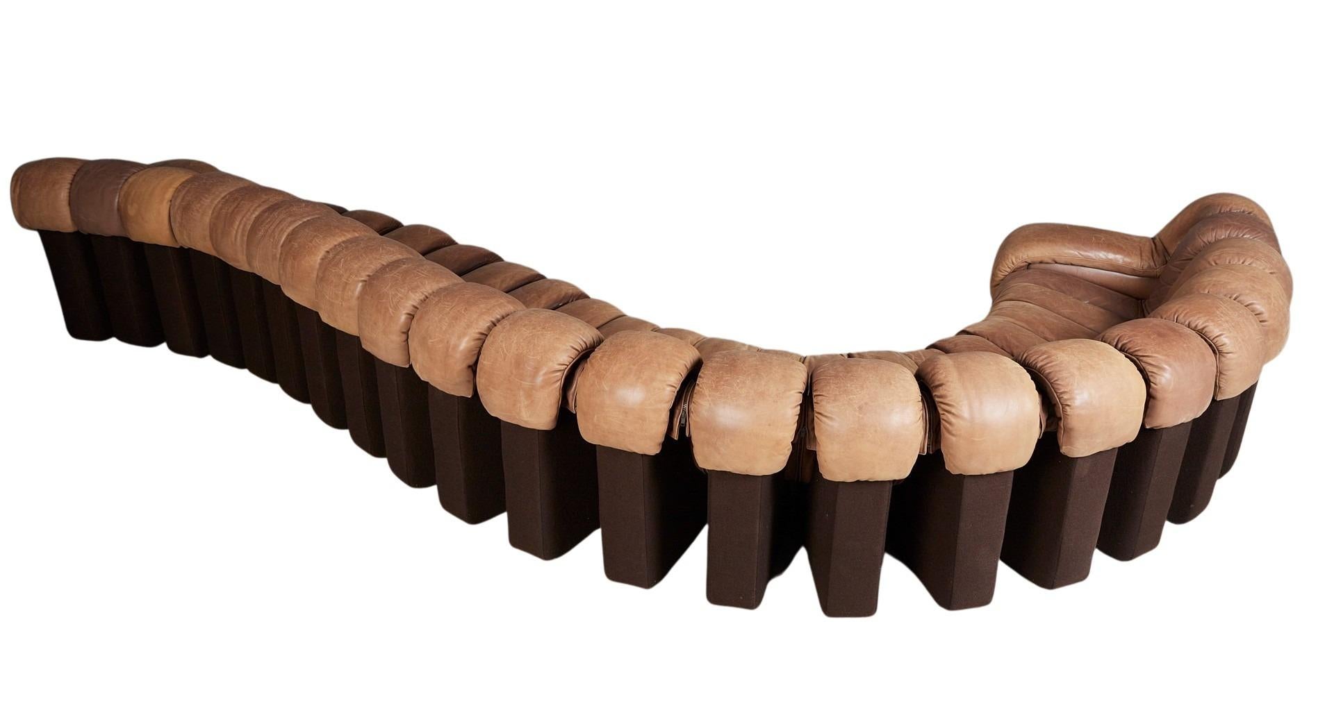 Striking modular sofa system composed of 22 L-shaped armchair modules, including two sculptural end pieces. Each unit features a plush, upholstered seat and backrest wrapped in rich cognac leather, with a dark brown felt underside for a refined