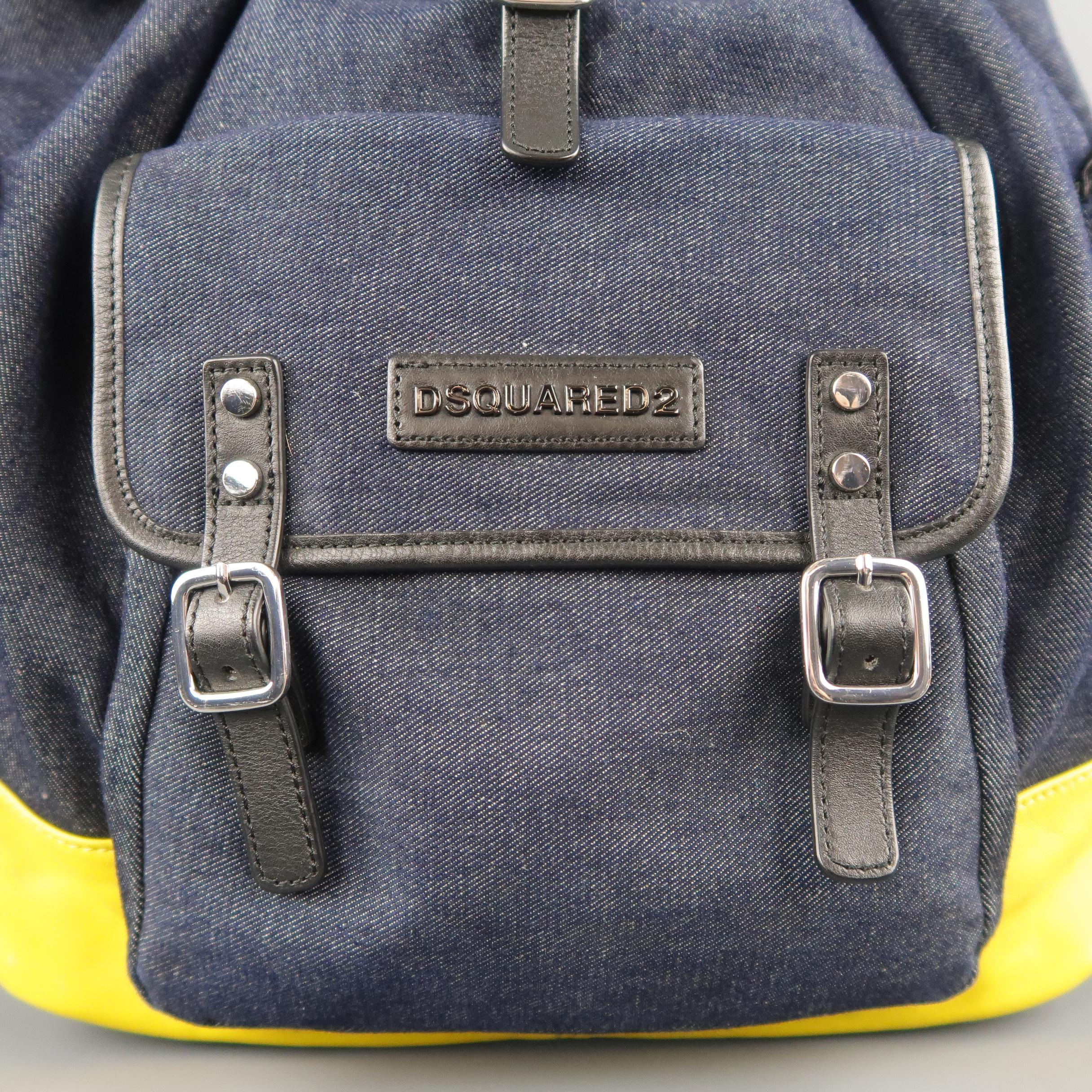 DSQUARED2 backpack comes in deep navy denim with black leather piping, side flap pockets, frontal pouch flap pocket with belt closures and logo, drawstring top with flap belt closure, top handle, and yellow leather bottom panel. Light wear on yellow