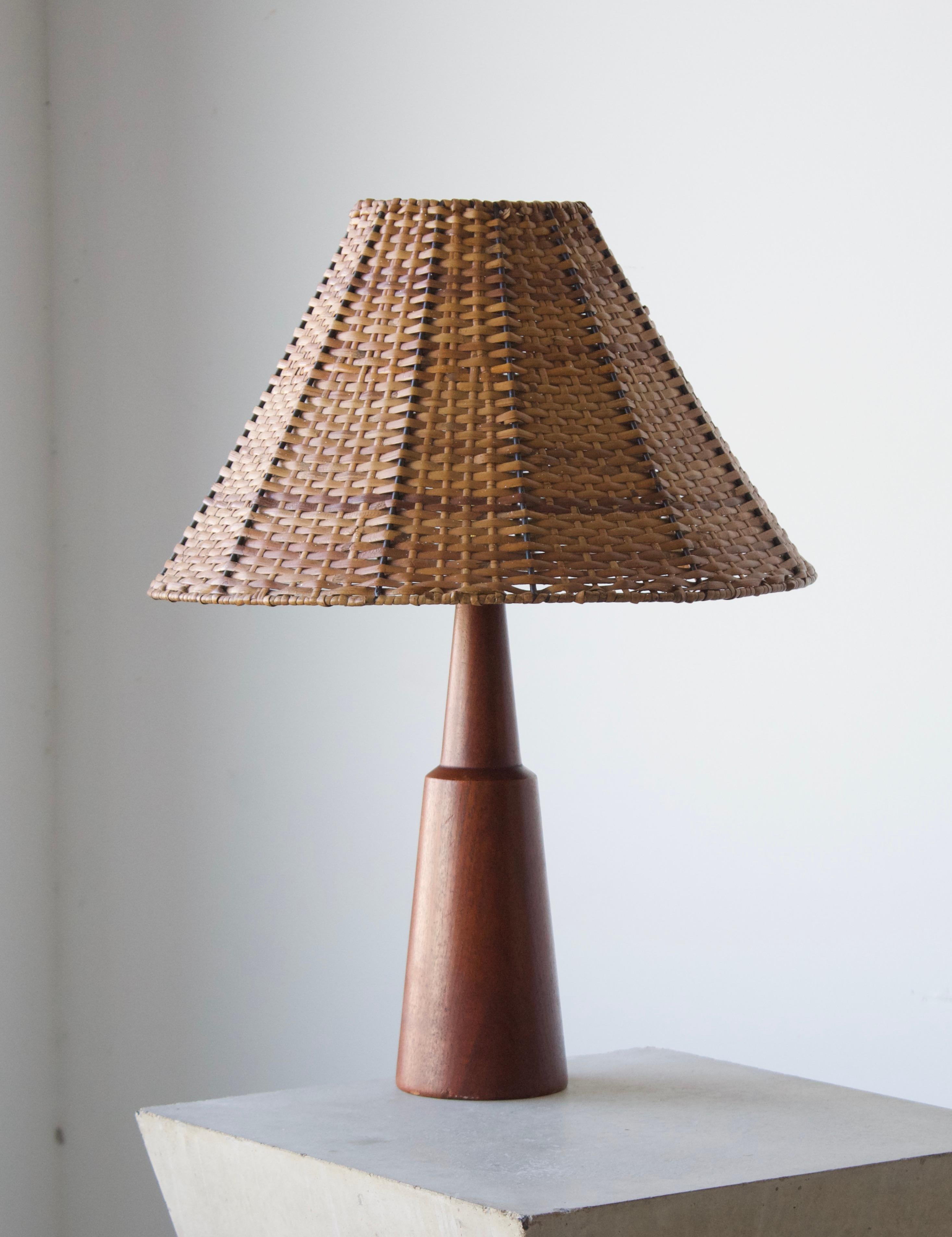 A table lamp, designed and produced in Denmark, 1950s. Features solid teak with brass inlays. 

Stated dimensions exclude lampshade, height includes socket. Illustrated model vintage rattan lampshade can be included upon request.