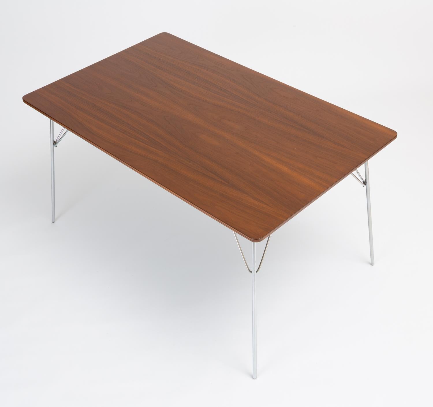 A rectangular dining table with walnut veneered surface and folding metal legs, designed by Ray and Charles Eames and produced by Herman Miller. Dubbed the DTM-10 (“Dining Table Metal”), this example was part of a series of tables introduced in 1947