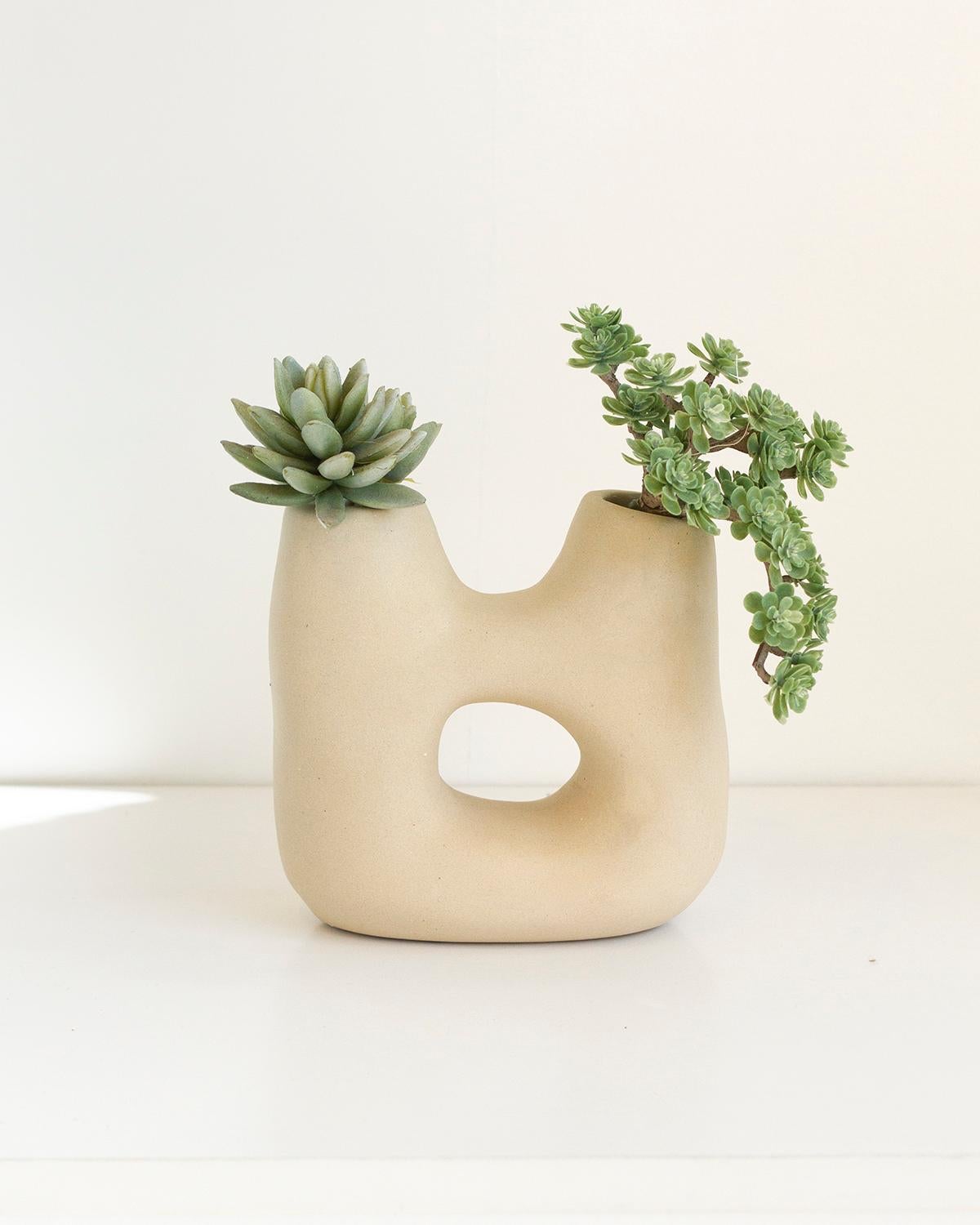 Diese moderne, organische Vase aus beigem Ton mit zwei Öffnungen ist das perfekte Weihnachtsgeschenk. Sie ist robust und elegant. Sein stiller Luxus ist perfekt für ein minimalistisches Zuhause. Mit Sorgfalt handgefertigt, strahlt er Eleganz