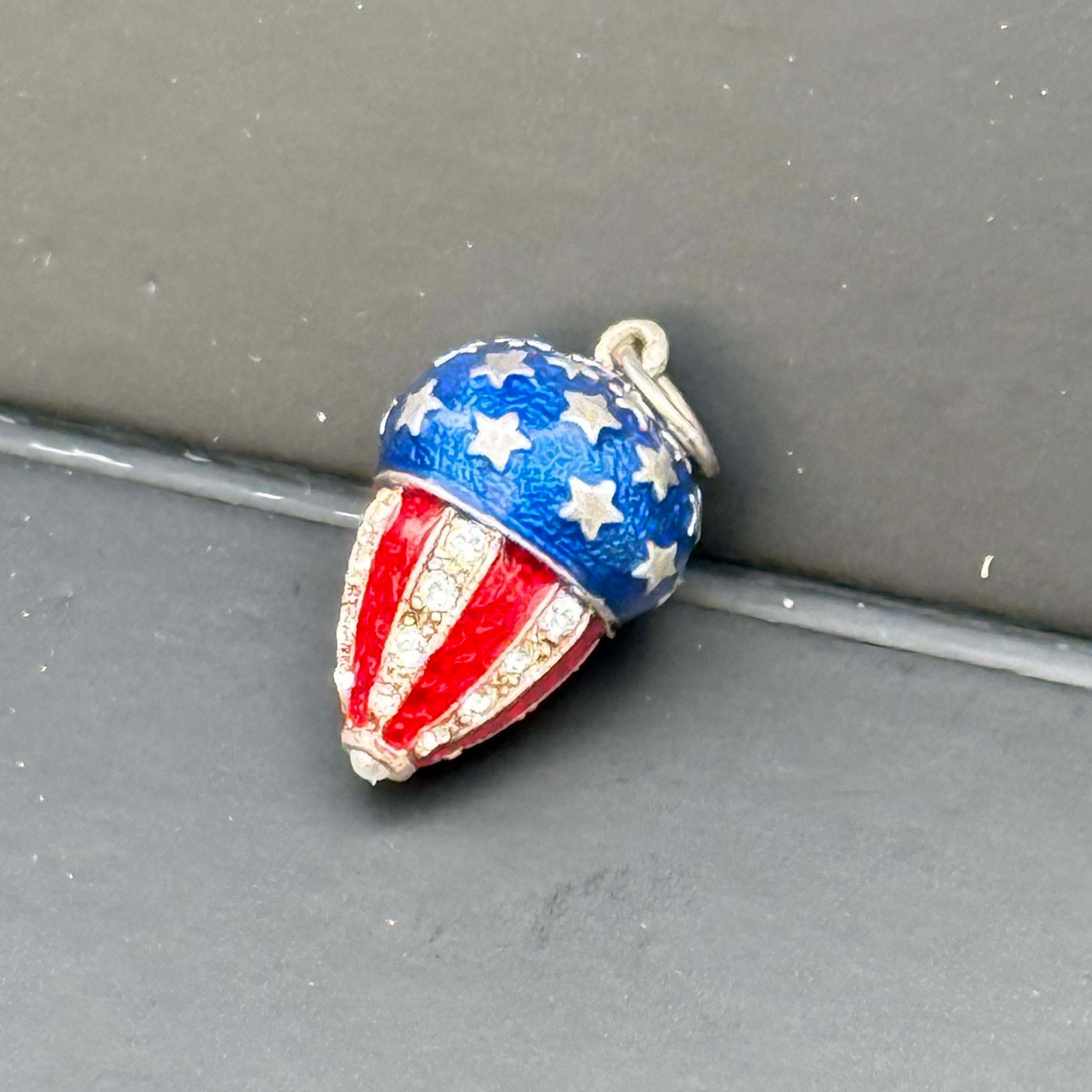 Questo squisito ciondolo vintage combina magnificamente il fascino patriottico con un'eleganza raffinata. Realizzato in argento sterling, il pezzo presenta un vibrante smalto rosso, bianco e blu che ricorda la bandiera americana, con file di strass