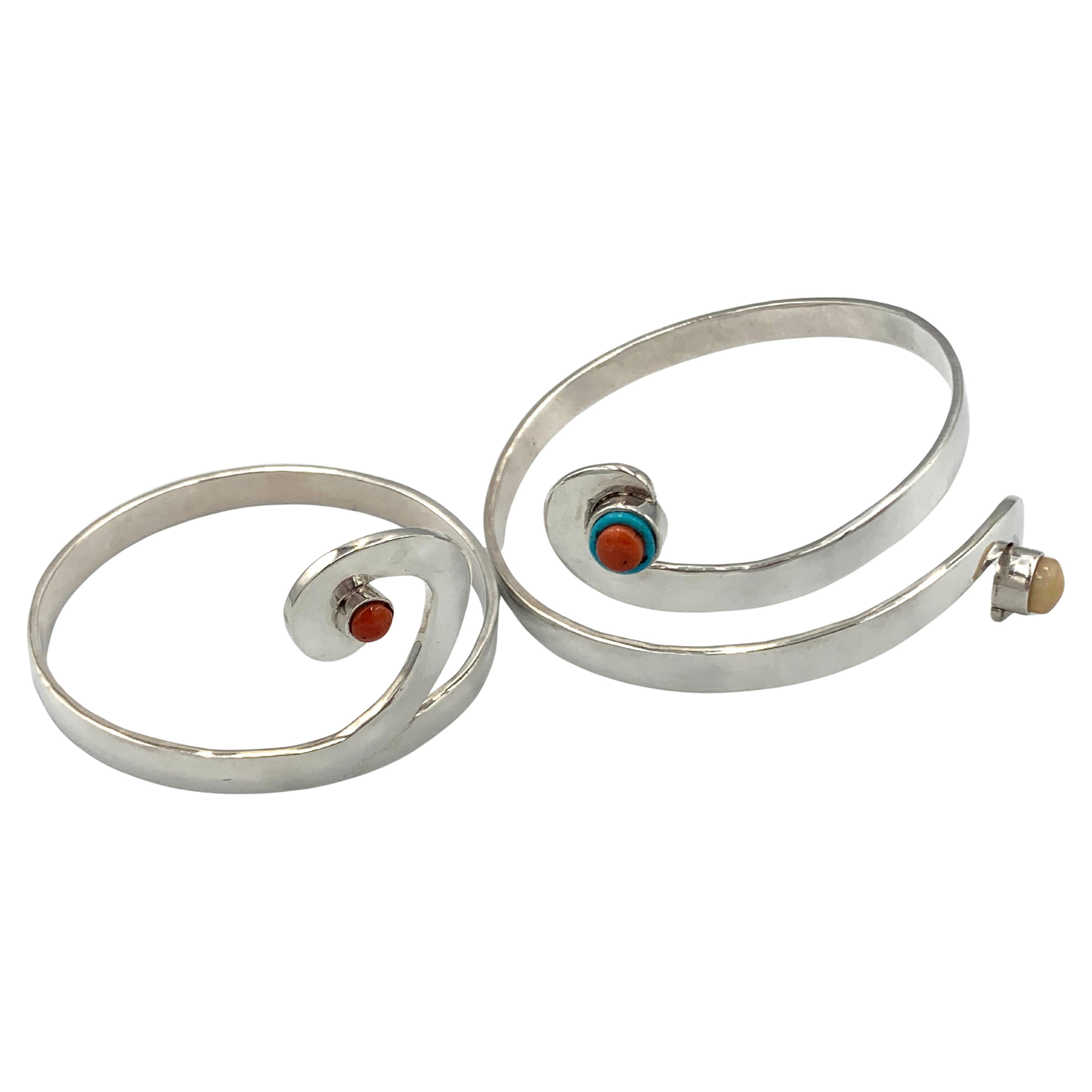 Puños dobles de plata de ley del talentoso orfebre pima Dylan Chiago. El brazalete de la parte superior del brazo tiene adornos de coral, turquesa y ópalo. El brazalete inferior del brazo tiene una pequeña piedra de coral. 

El puño superior es