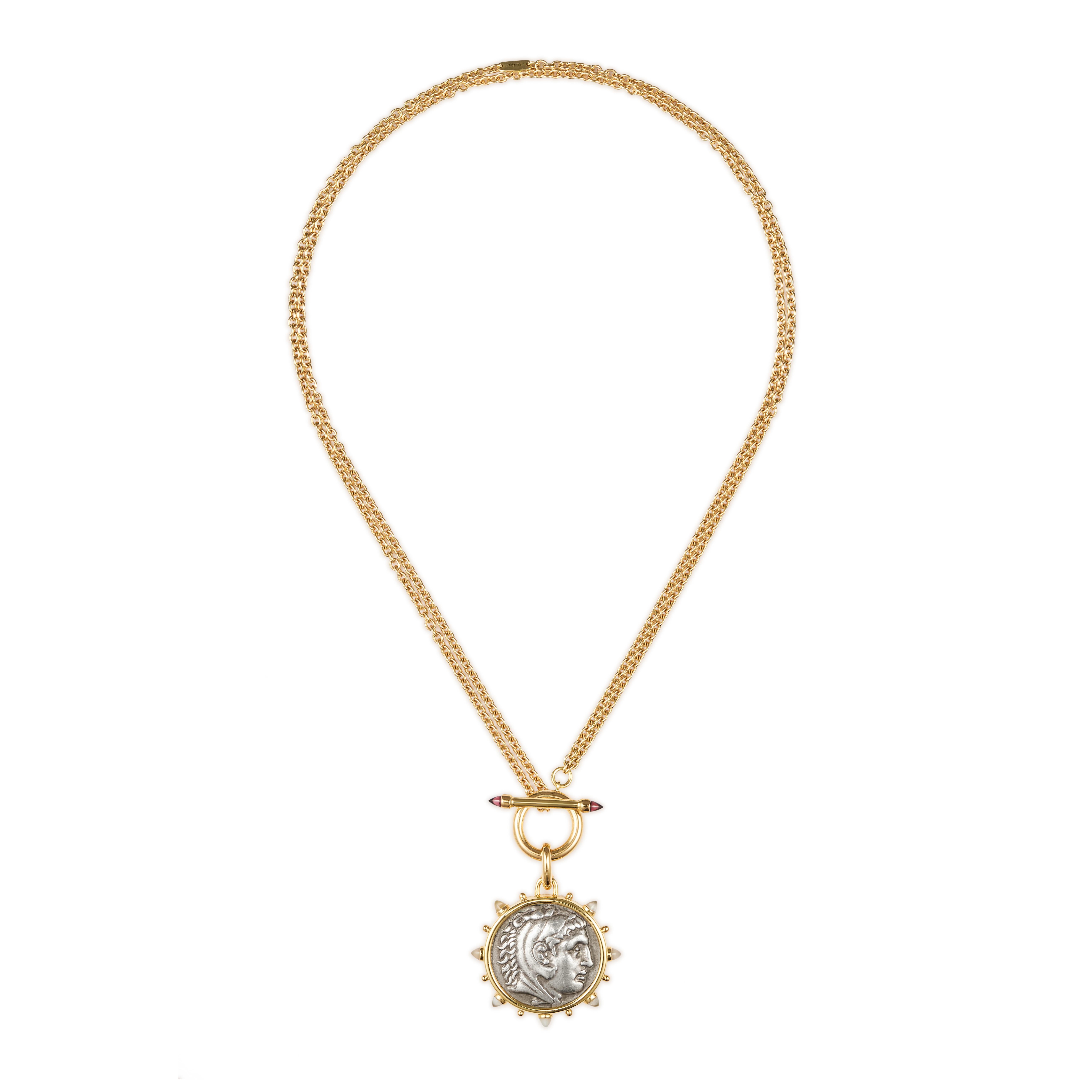 This DUBINI coin necklace from the 'Empires' collection features an authentic Macedon coin set in 18K yellow gold embellished with bullet moonstone cabochons, paired with a unique rollo chain front closing toggle featuring rhodolite garnet