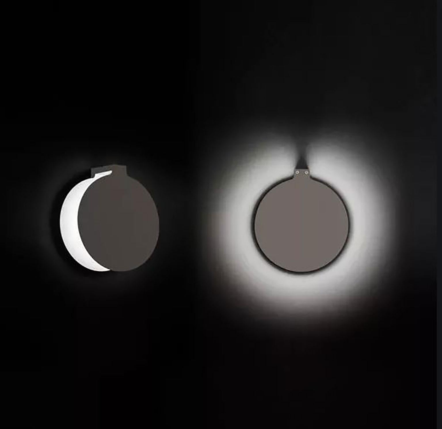 Duca wall lamp designed by Nicola Gallizia for Oluce. Elegant and dramatic, the light from this fixture is revealed differently to the observer depending on where you are standing and an almost lunar eclipse in progress is revealed as one walks