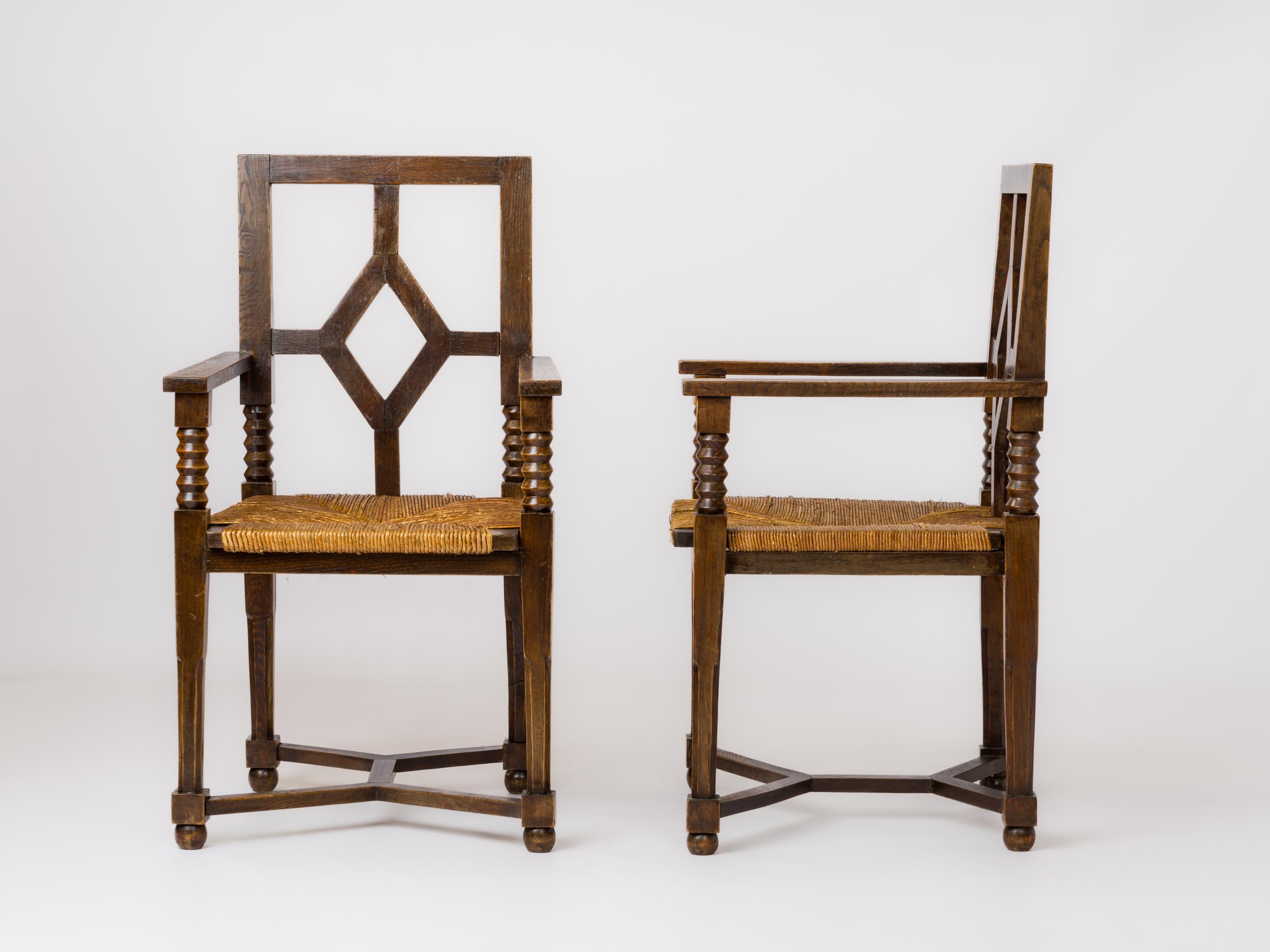 Pair of regionalist armchairs in stained oak with straw seats. 
In the style of Charles Dudouyt.
Backrest with diamond pattern. Inverted double U-shaped crossbars.
In good vintage condition. Minor structural damages on rush.
These chairs will ship