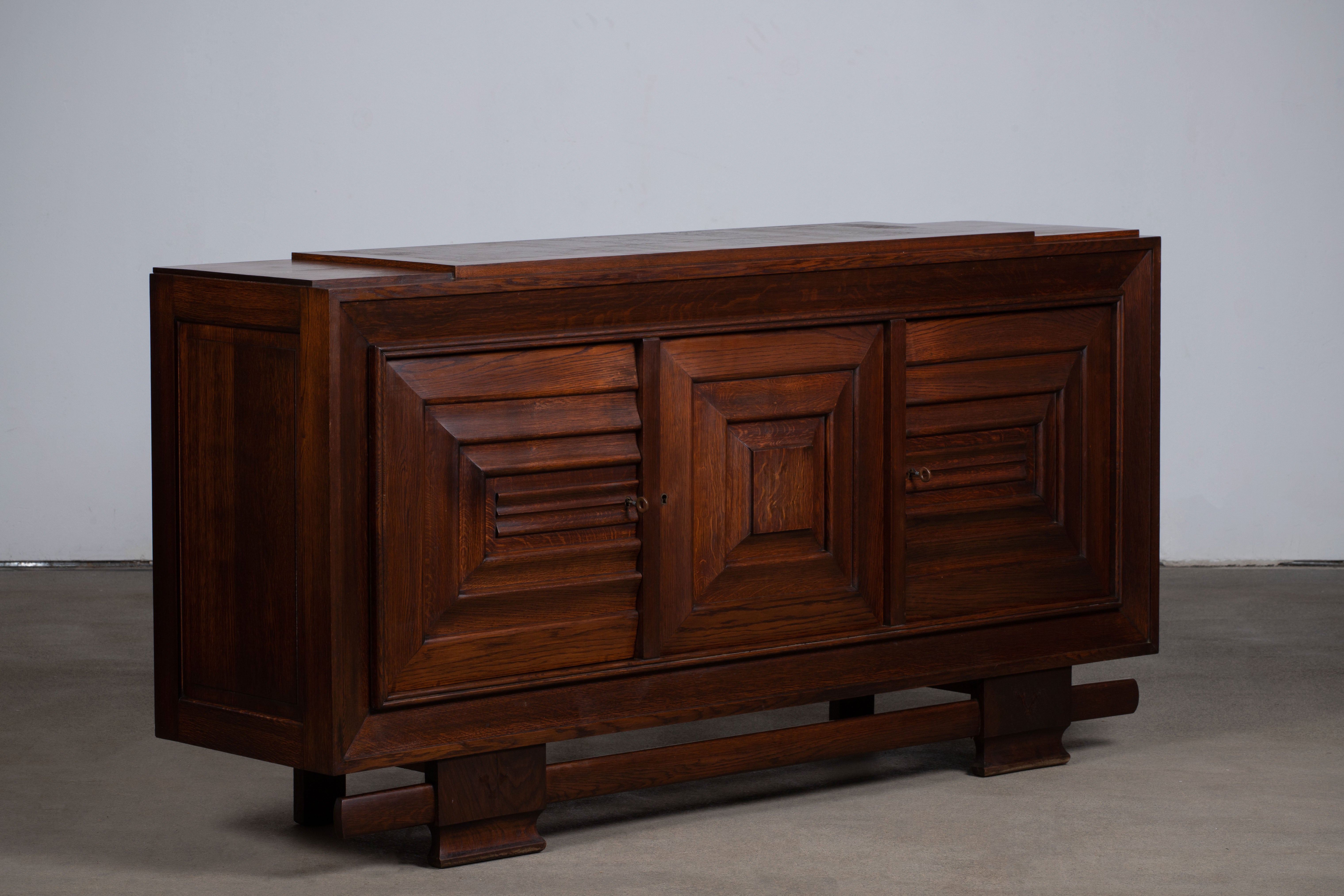 Credenza, solid oak, France, 1940s, attributed to Charles Dudouyt.
Large Art Deco Brutalist sideboard. 
The credenza consists of three storage facilities and covered with very detailed designed door panels. 
The refined wooden structures on the