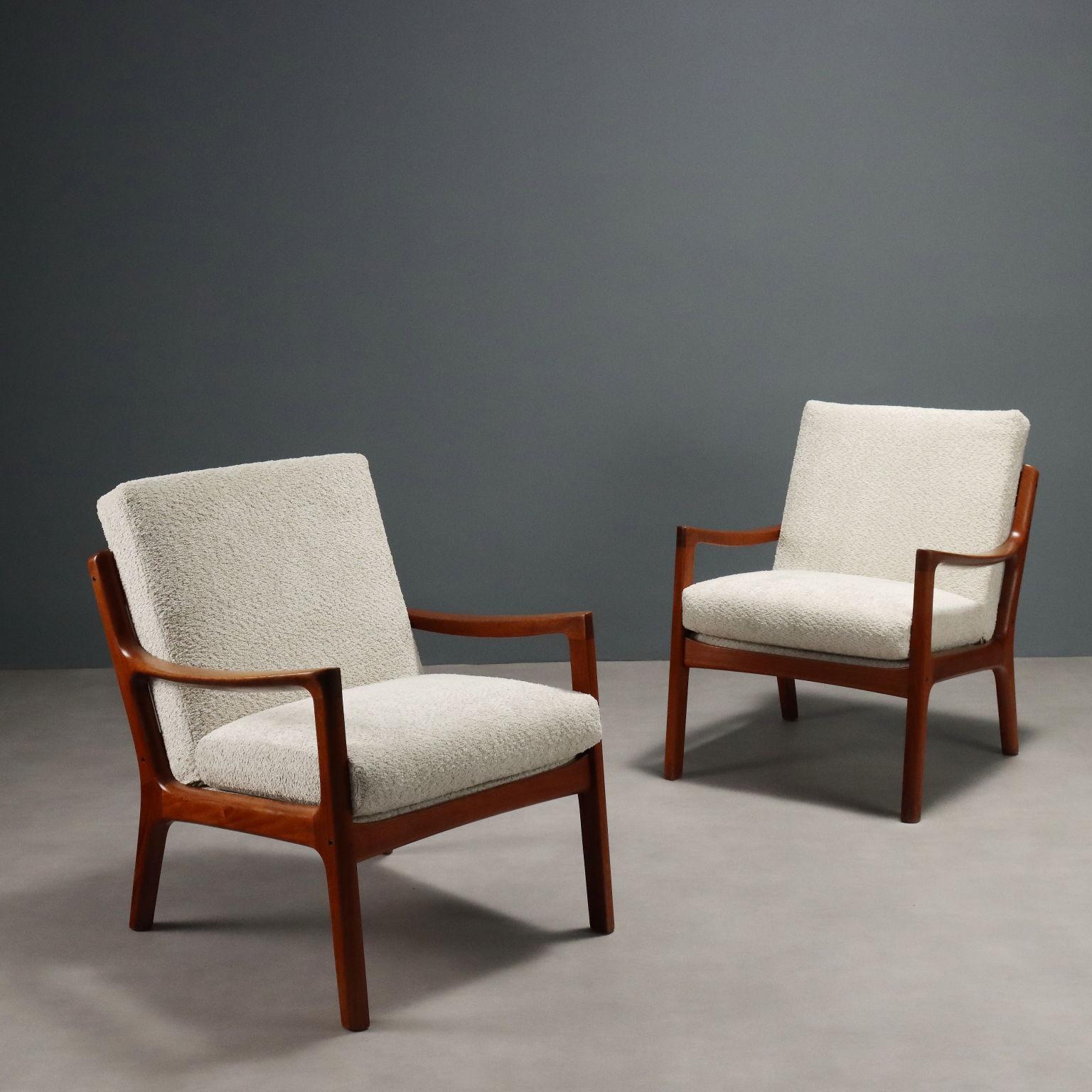 Coppia di poltrone vintage con struttura in legno di teak a vista, seduta e schienale con imbottitura in espanso e molle, tappezzeria nuova in tessuto bianco. Presente il marchio della manifattura.
