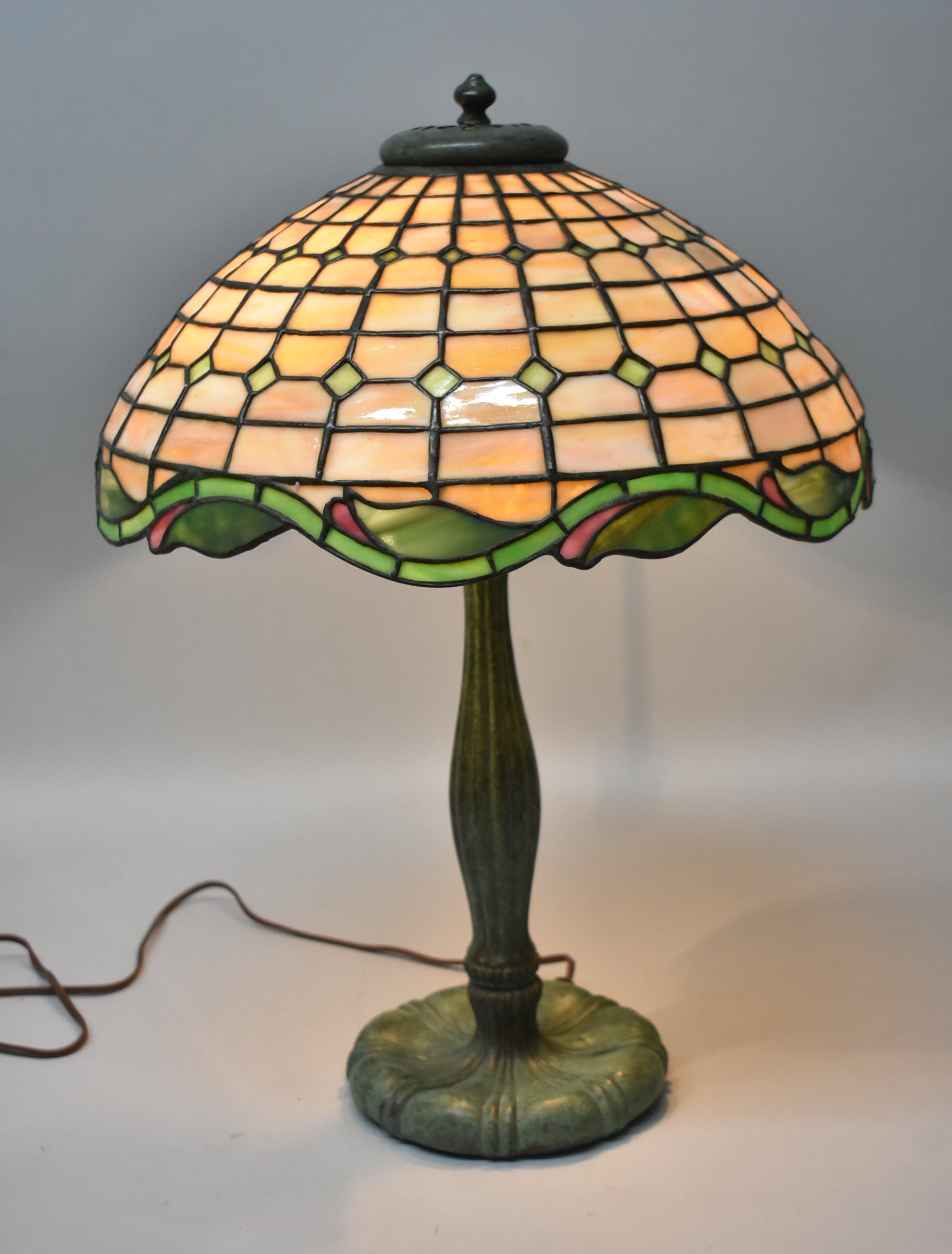 Diese wunderschöne Bleiglaslampe von Duffner & Kimberly aus dem Jahr 1910 hat einen 16-Zoll-Schirm mit einem geometrischen Muster in Bernsteintönen und einem gewellten Rand in sattem Grün. Sie hat eine belüftete Wärmekappe. Der Originalsockel weist