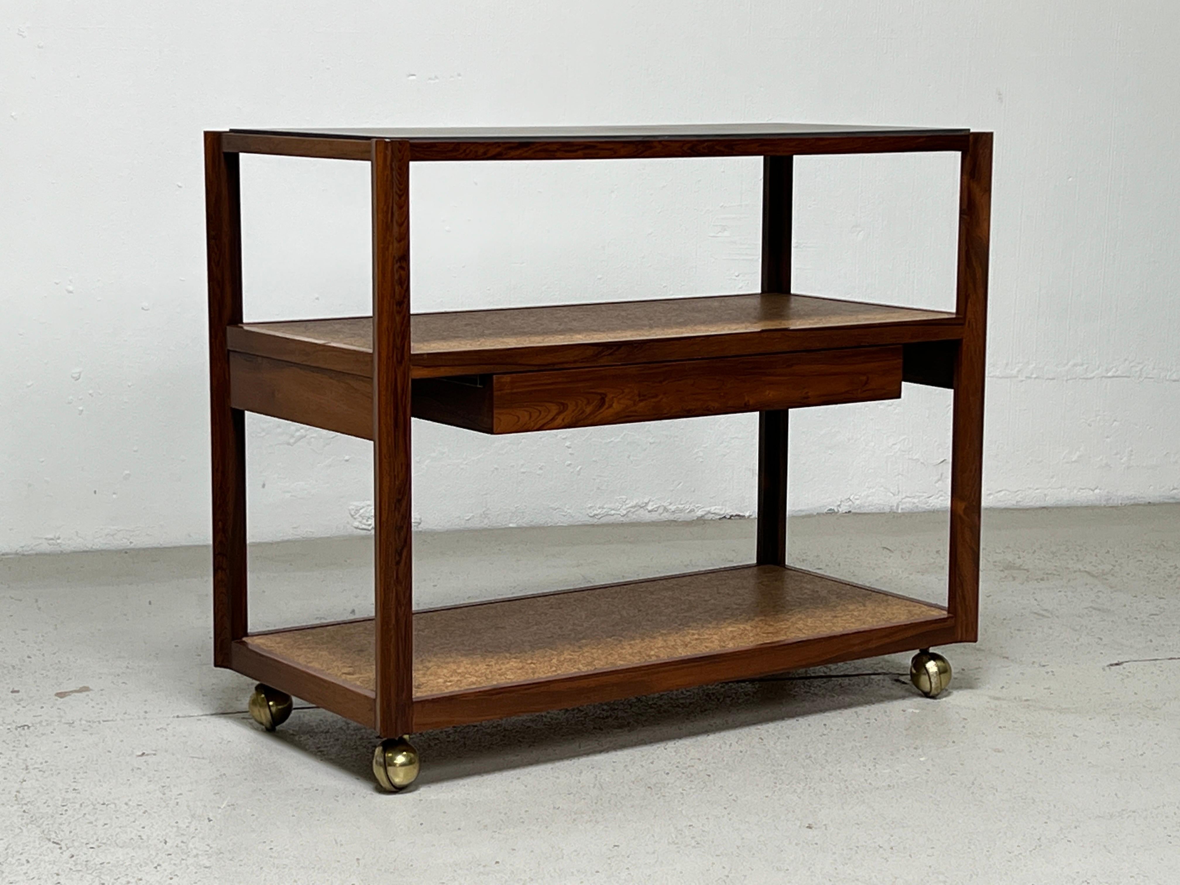 A sculpted rosewood bar cart with single drawer, cork shelves and slate top. Designed by Edward Wormley for Dunbar.