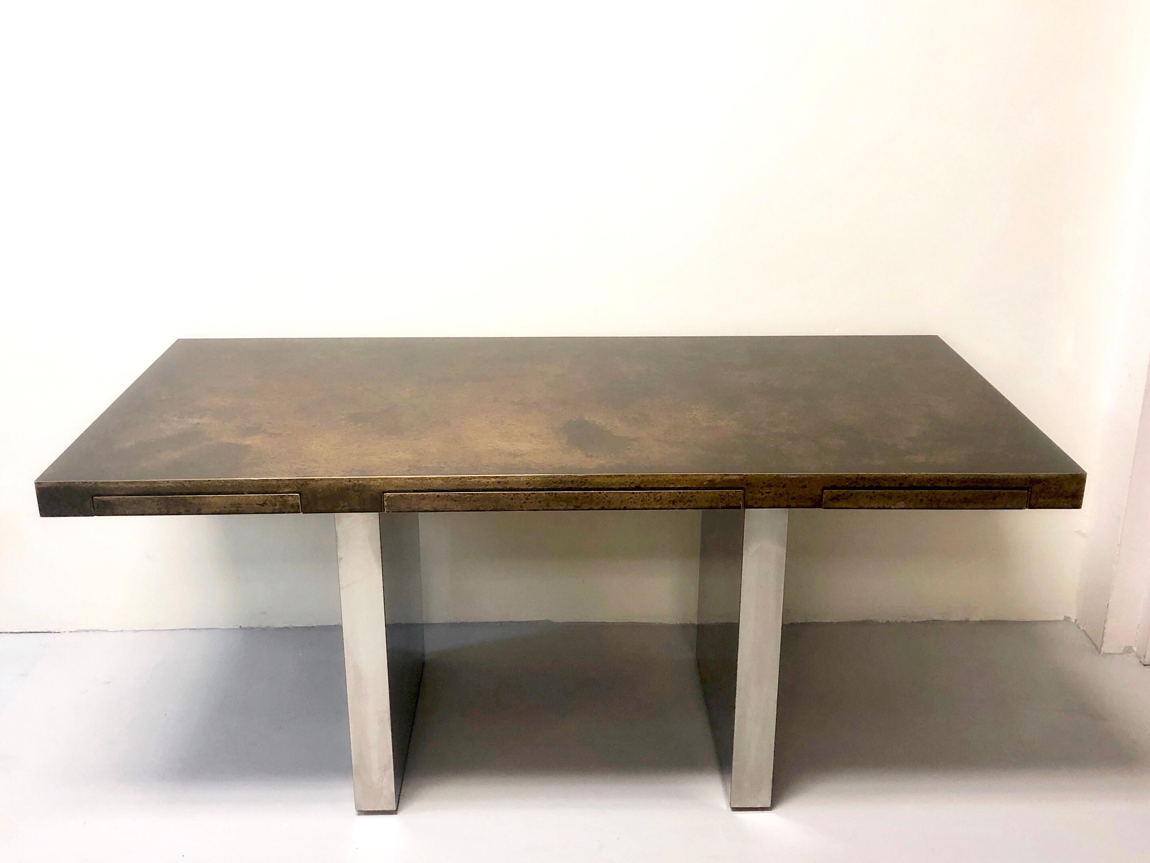 A slim Dunbar desk with very clean lines and wonderful patinated brass top. 2 monolithic bases in stainless steel. There are 3 drawers with pencil canoes very slim and deep.