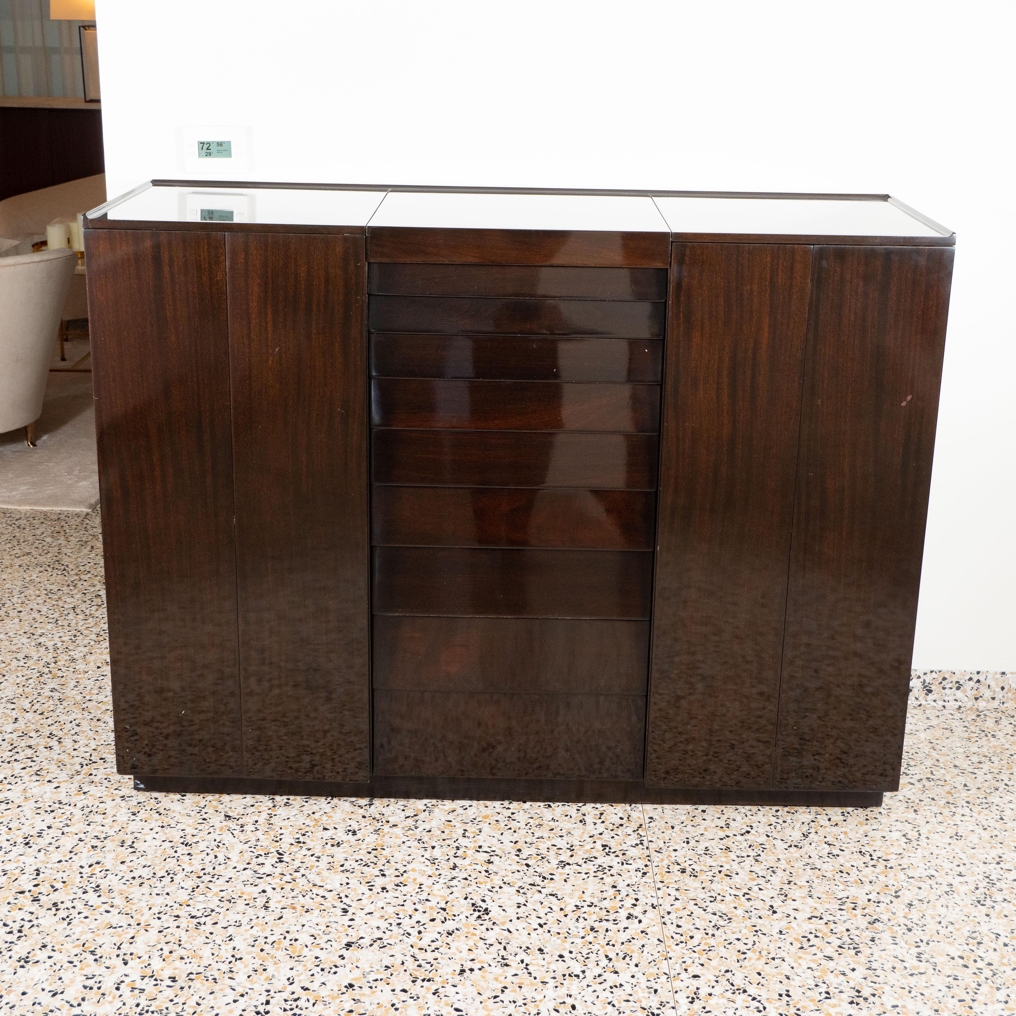 Edward Wormley for Dunbar Gentleman's Chest, a mid-century modern dressing cabinet.

USA, circa 1950.

Crafted of dark stained walnut with the rectangular top centering a lifting mirrored vanity panel, above nine concealed ziggurat drawers,