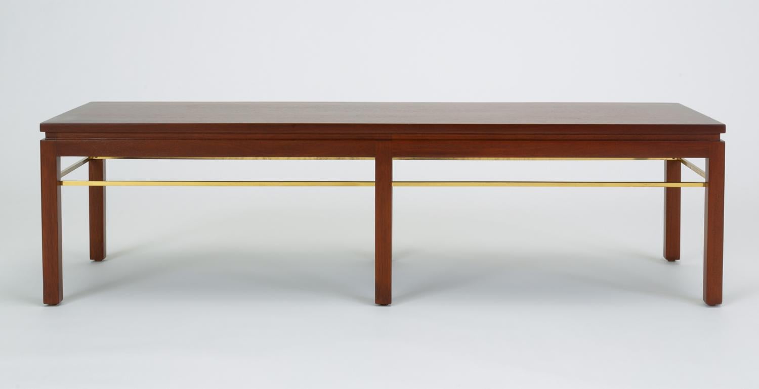 A long, rectangular coffee table designed by Edward Wormley for Dunbar. The model 313 has six square post legs that sit flush with the corners of the piece. Each leg is notched to fit a brass stretcher that defines the interior edges of the table.