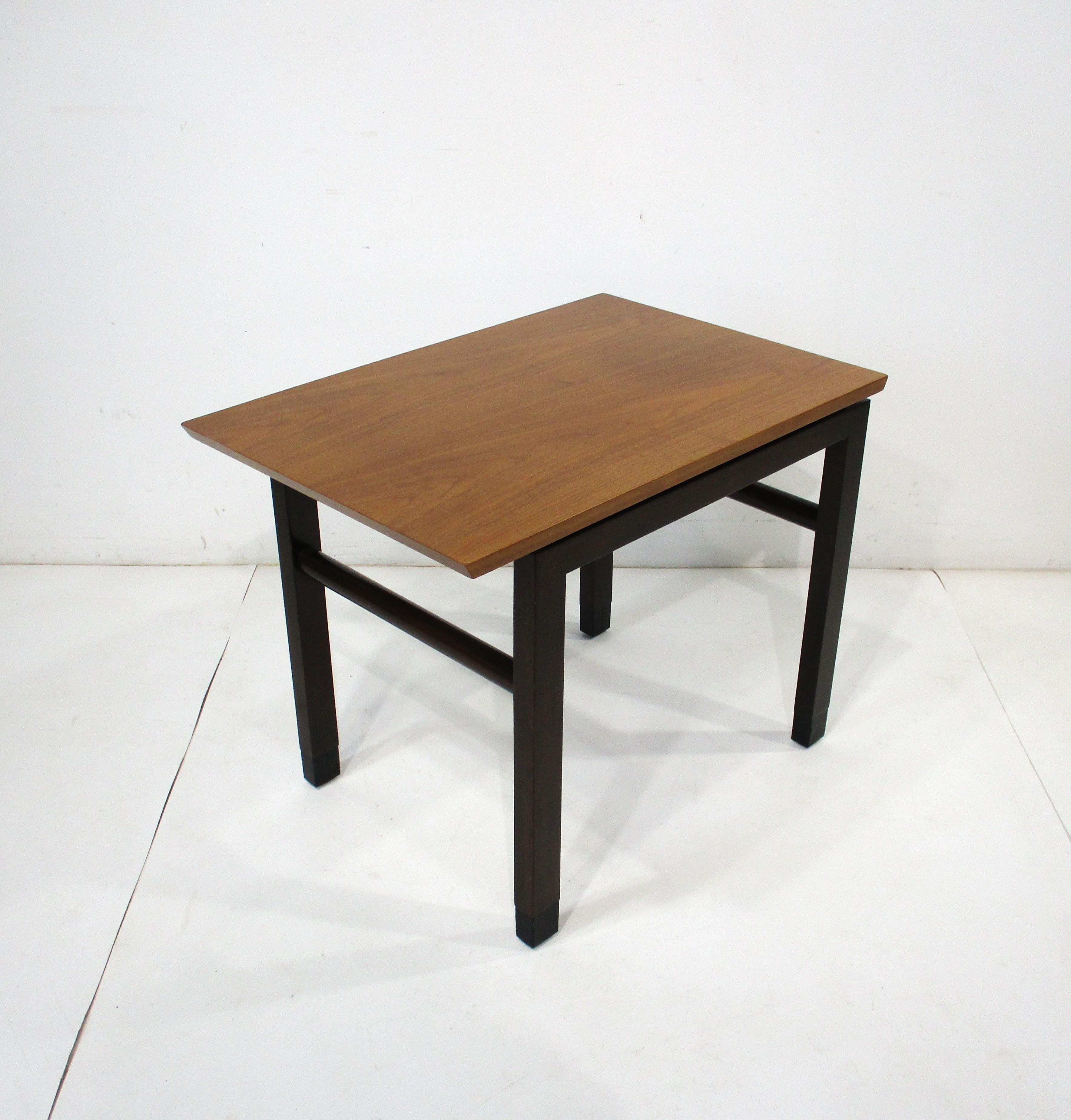 A nice single walnut topped side end table with dark ebony toned legs and stretchers and black leather wrapped leg tips . The cantilevered top presents splendidly with the other design cues of the piece that the designer Edward Wormley was noted for