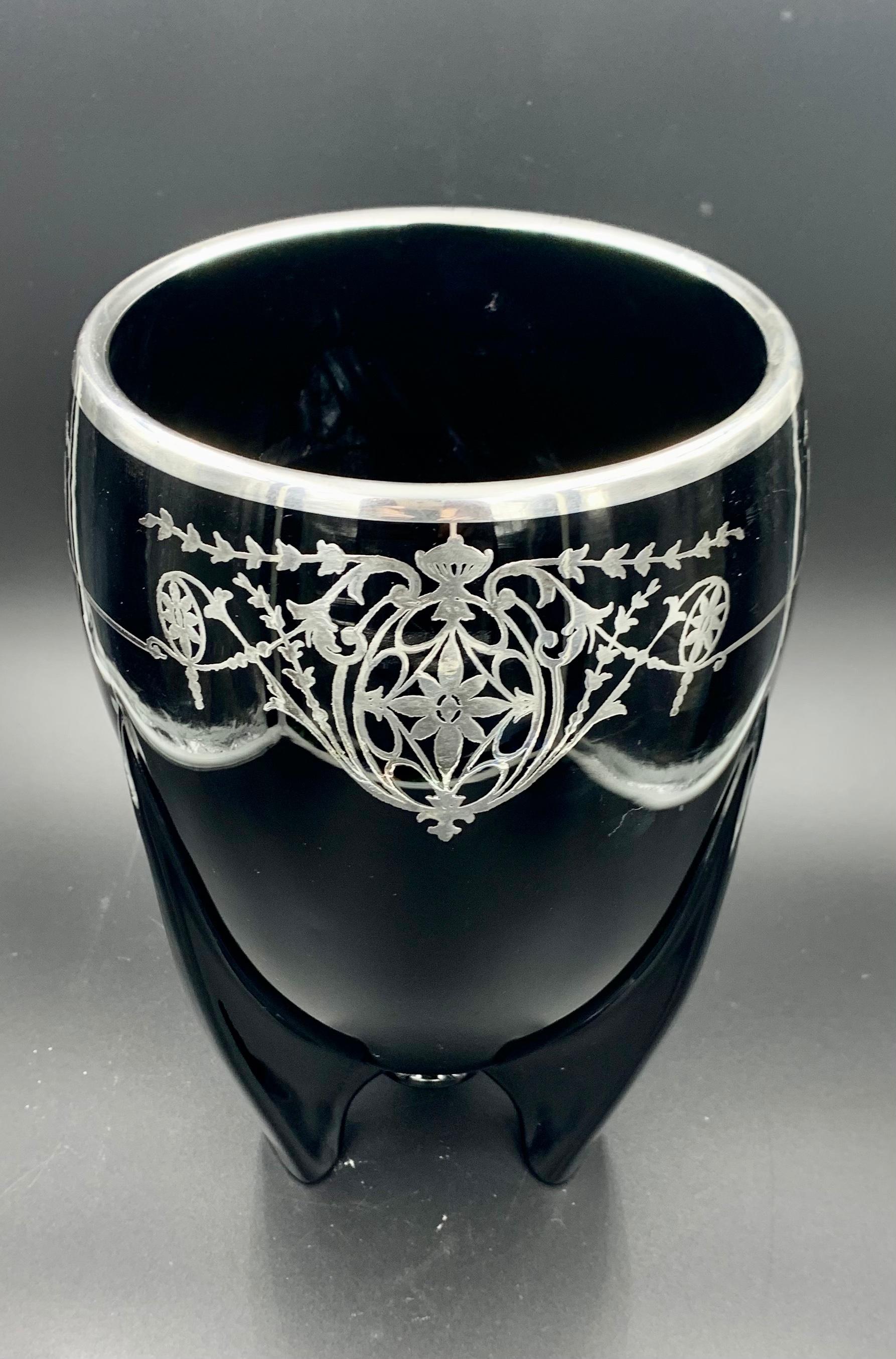 This striking black rocket vase silver overlay made in the 1930s by Duncan Miller. It is made of heavy opaque ebony glass with a bright finish. The ornate sterling silver overlay pattern repeats three times around the vase featuring a flower and