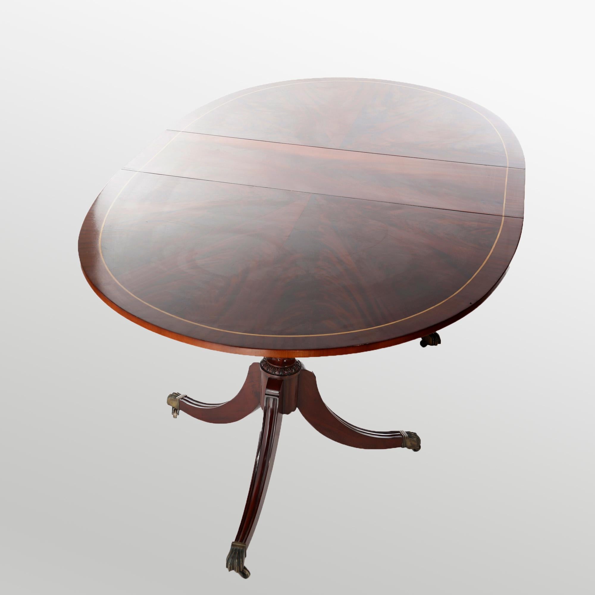 A Sheraton style extension dining table in the manner of Duncan Phyfe offers flame mahogany construction with top in oval form with cross banding and inlaid satinwood raised on double urn form pedestals with three legs terminating in cast paw feet,