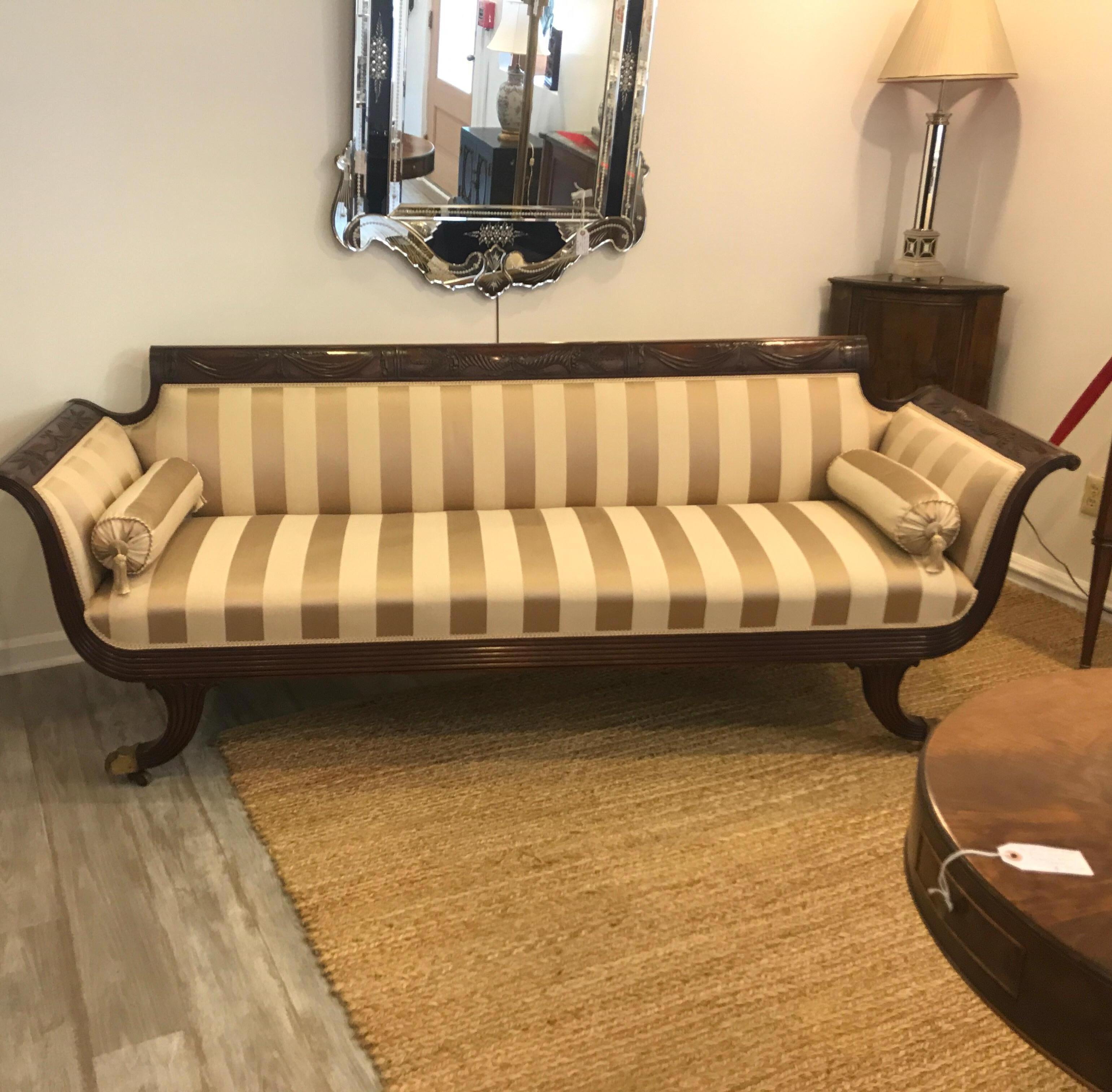 Elegant hand carved mahogany Duncan Phyfe style sofa with damask stripe upholstery. The attached back and seat, with nicely finished back with two tasselled round bolster accent pillows. Has the original brass capped feet and castors.