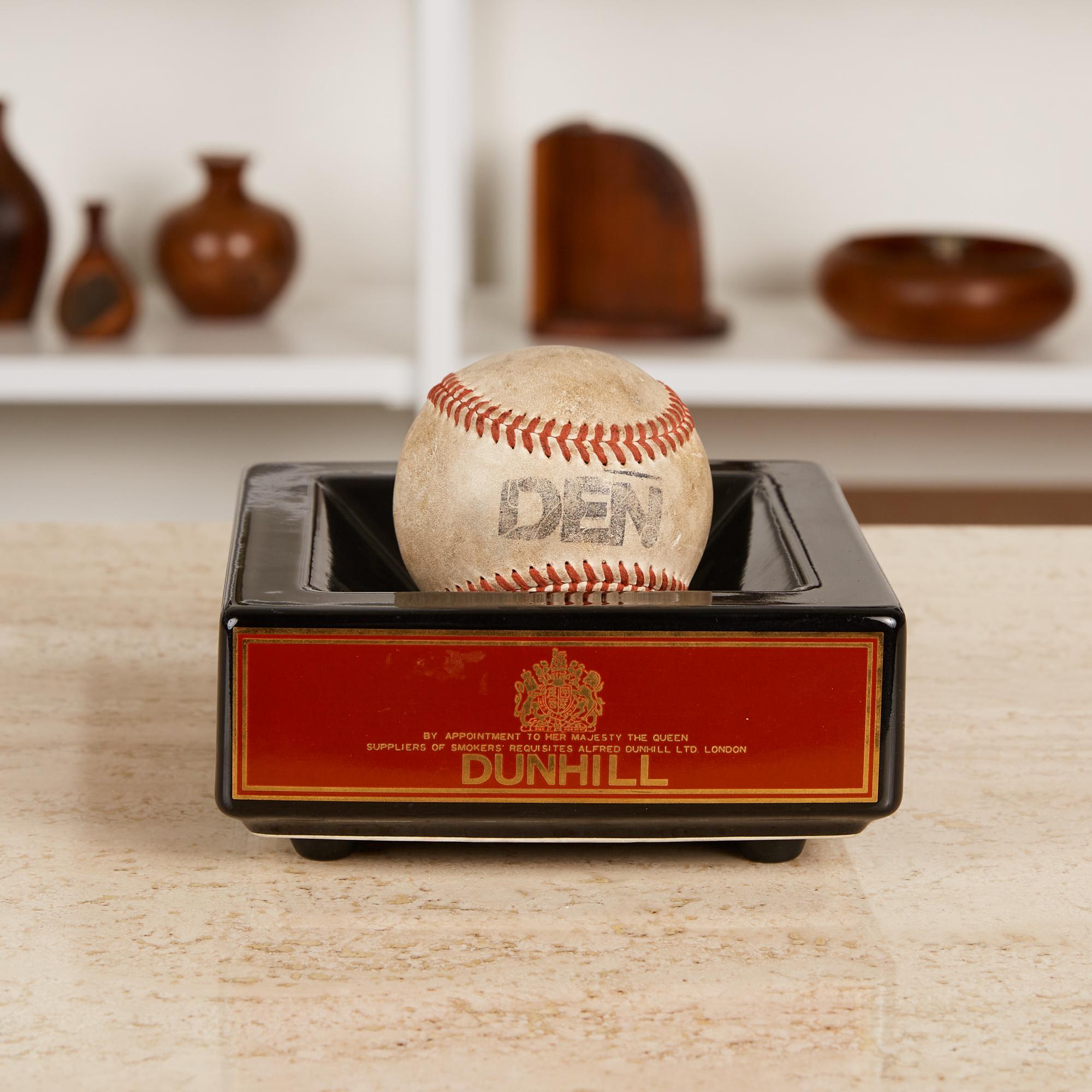 Square ceramic ashtray with black high gloss glaze, features red and gold Dunhill label on all four sides. Has four small feet to elevate it off a table surface. 

Dimensions: 5.75” width x 5.75” depth x 2.55” height. 

Condition: Excellent