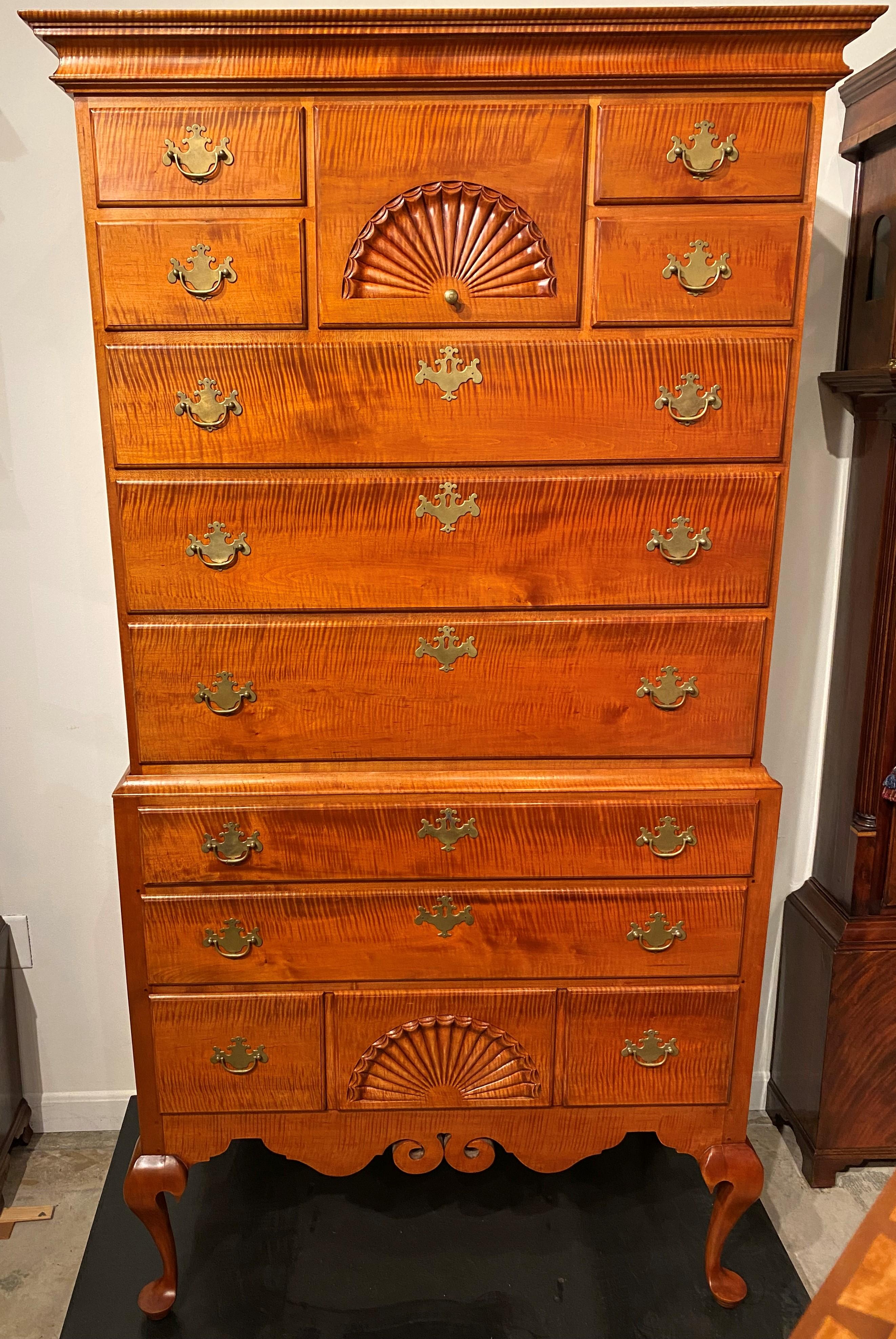 A fine example of a bench made two part tiger maple highboy made in the Dunlap style, its upper case with a molded cornice surmounting a central drawer with radial fan carving flanked by two fitted drawers on either side, over three long drawers,