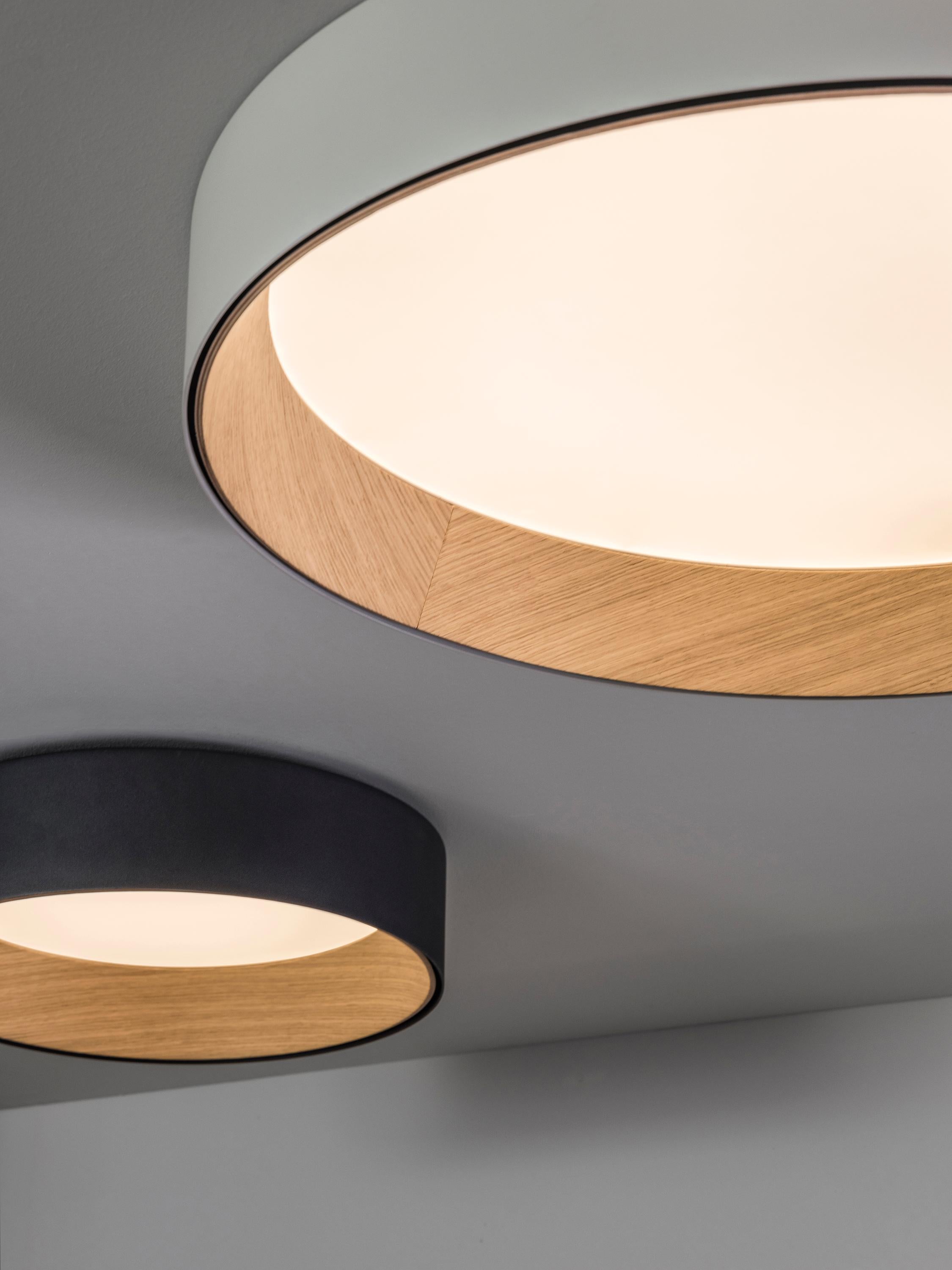 La collection DUO s'inspire de la durabilité et du bien-être. Cette lampe de surface encastrée est conçue pour les endroits où le plafond est plus bas. La surface intérieure de l'abat-jour est revêtue d'un placage de chêne, enveloppé dans une coque