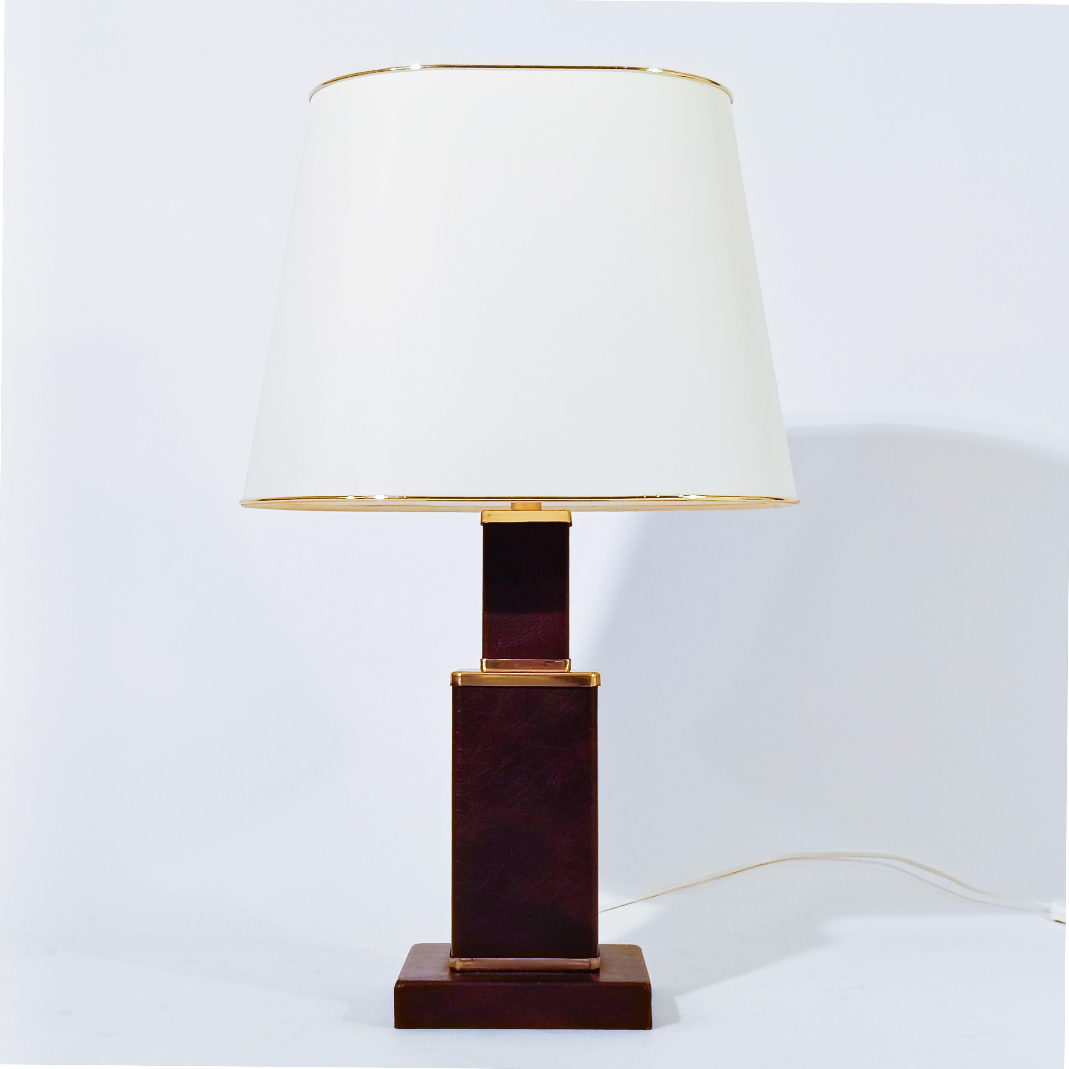 Art Deco and Hollywood Regency style table lamp, France, 1960s. Skyscraper-shaped table lamp made of faux leather and brass. Several prismatic levels and a cylindrical upper axis of gold chrome metal where the lamp holders are attached. Original