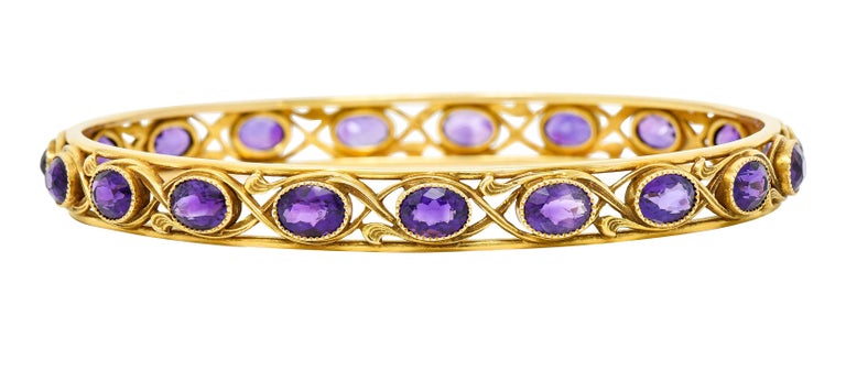 Bangle bracelet is bezel set fully around by oval cut amethysts

Saturated, well matched, while measuring approximately 6.0 x 4.5 mm

Stones are encompassed by meandering whiplash tendrils

Stamped 14K for 14 karat gold

Maker's mark for Durand &