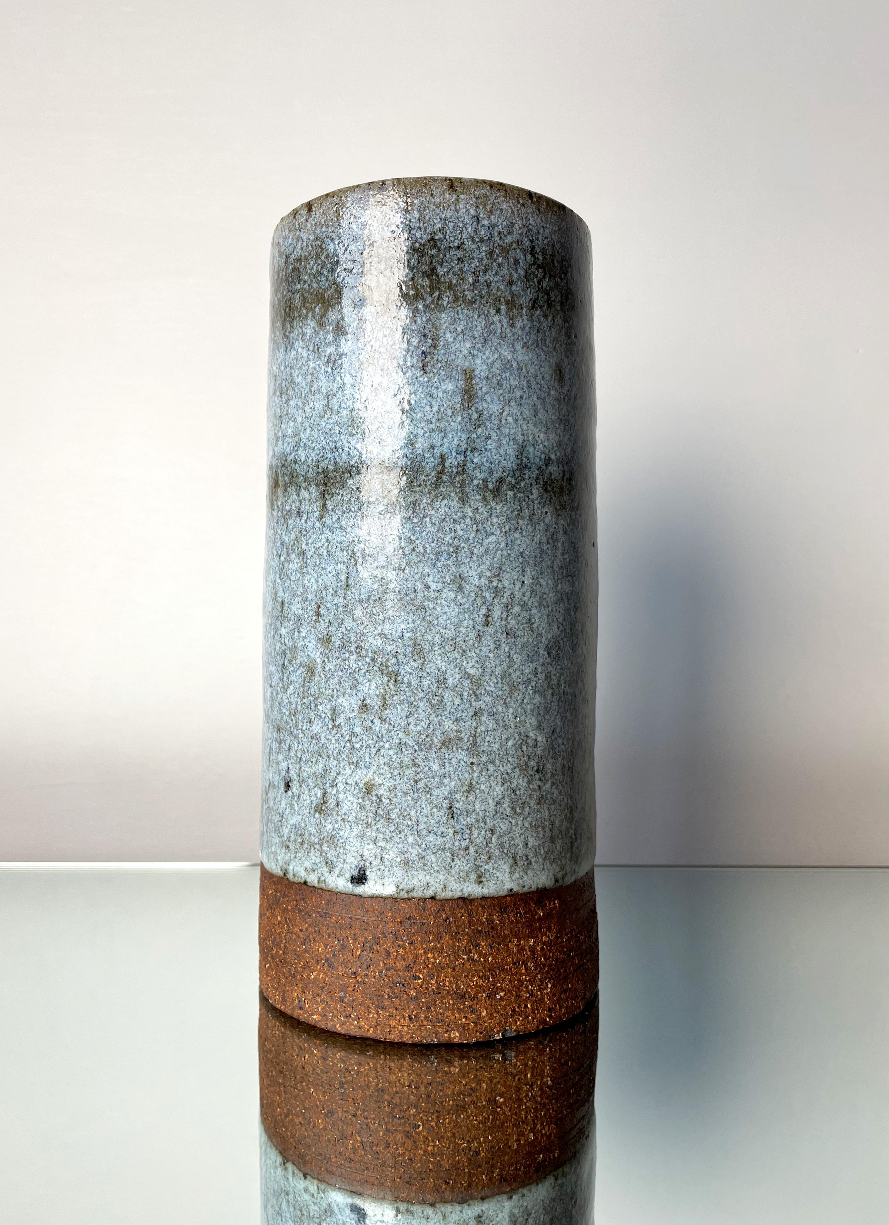 Handmade Danish midcentury modernist cylinder shaped stoneware vase from the 1960s. Dusty pastel blue and black speckled running glaze inside and out with two subtle dark blue lines on the top part of the vase. Raw unglazed base. Signed under base.