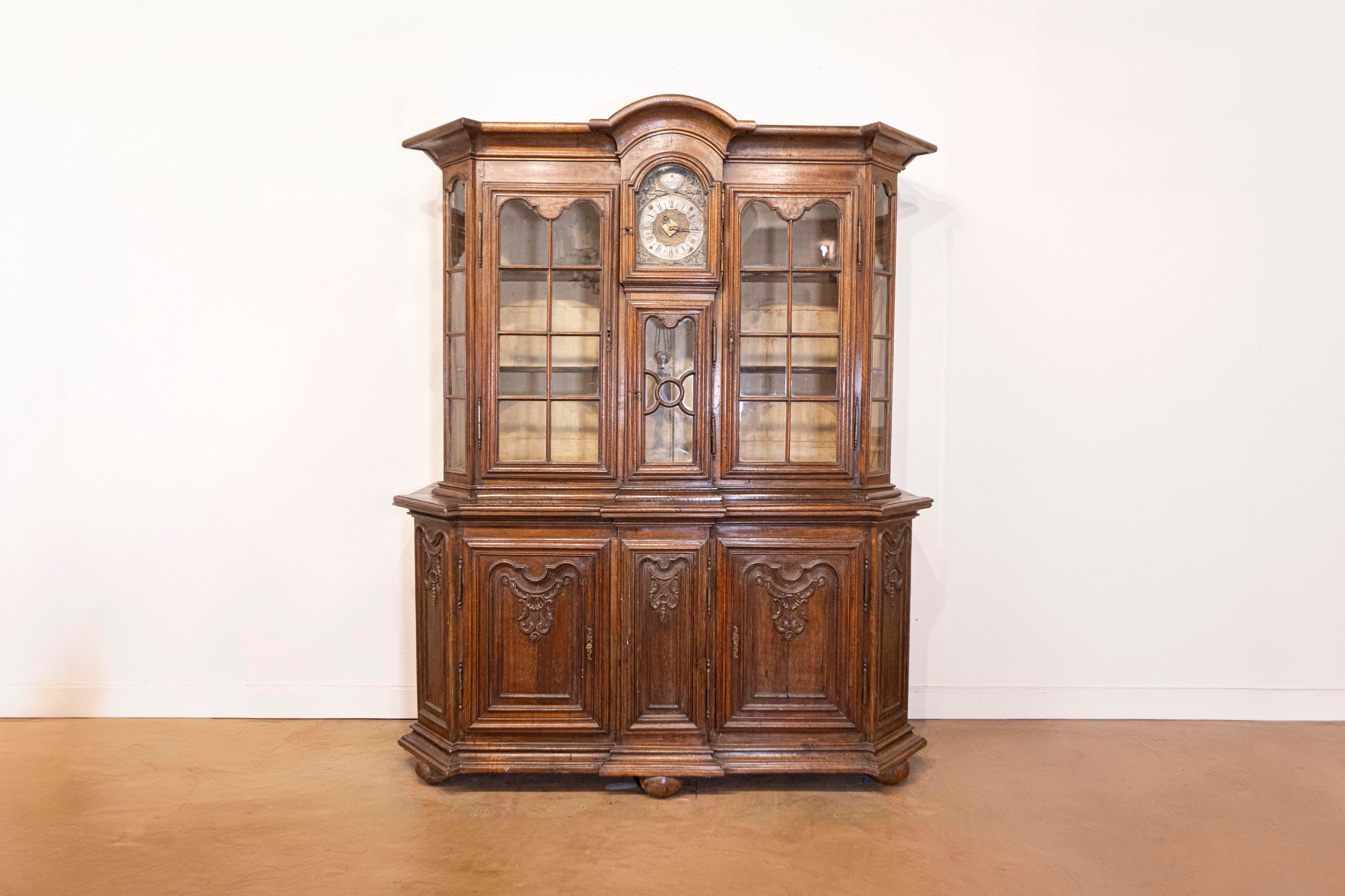 A Dutch oak buffet à deux-corps from the late 18th century, with glass doors, canted sides, carved panels and central clock. Born in the Netherlands during the last decade of the 18th century, this oak buffet à deux-corps features a bonnet-shaped
