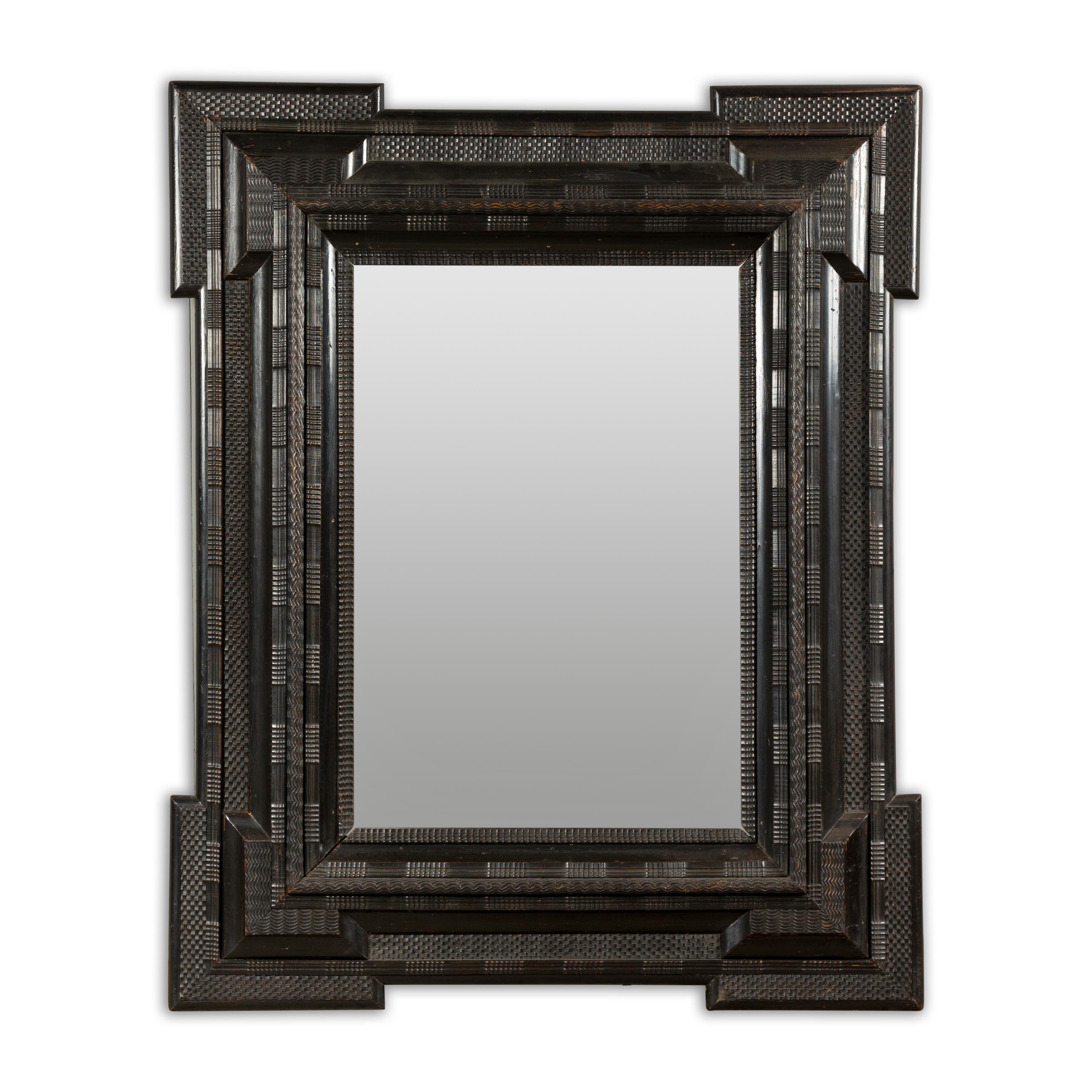 A large Dutch dark brown/black wall mirror from the 18th century with carved frame, protruding corners and geometric décor. Elevate your space with the timeless elegance of this large Dutch dark brown/black wall mirror from the 18th century. Crafted