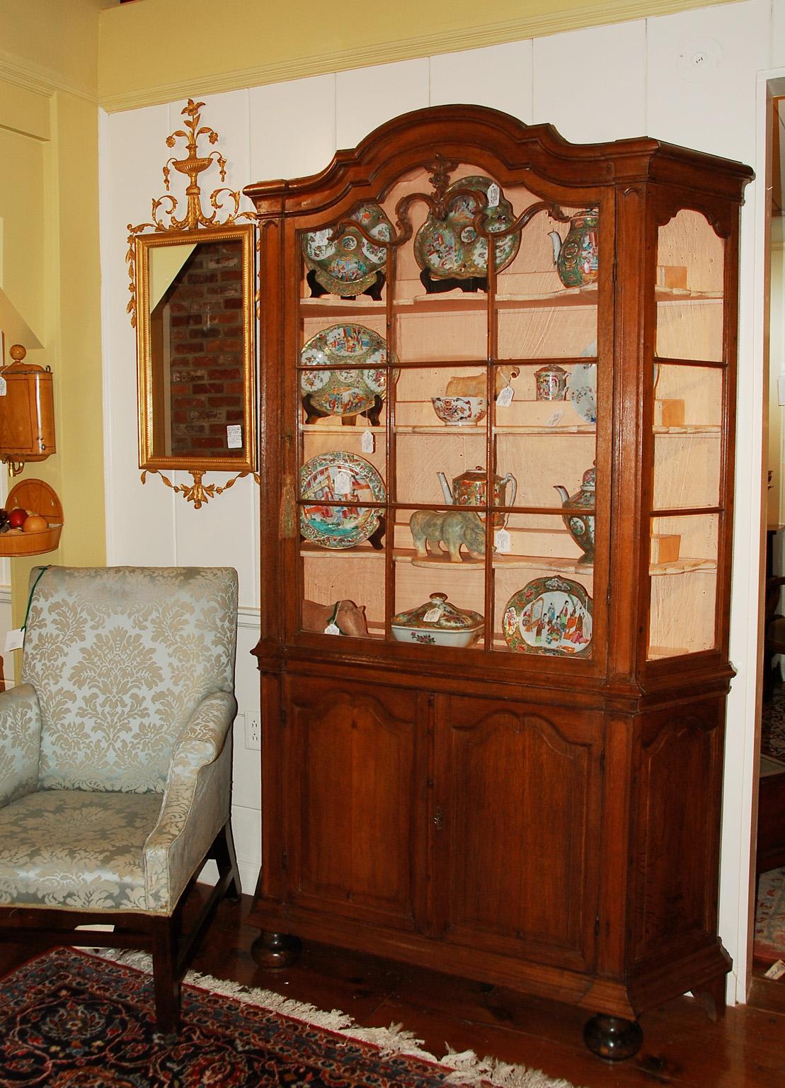 Dutch oak glazed top, two part display cabinet with bold moldings, astragal glazed glass panes surmounted by carved leaf moldings extending into the top cresting frame of the shaped central door. The lower part of the cabinet is enclosed by four