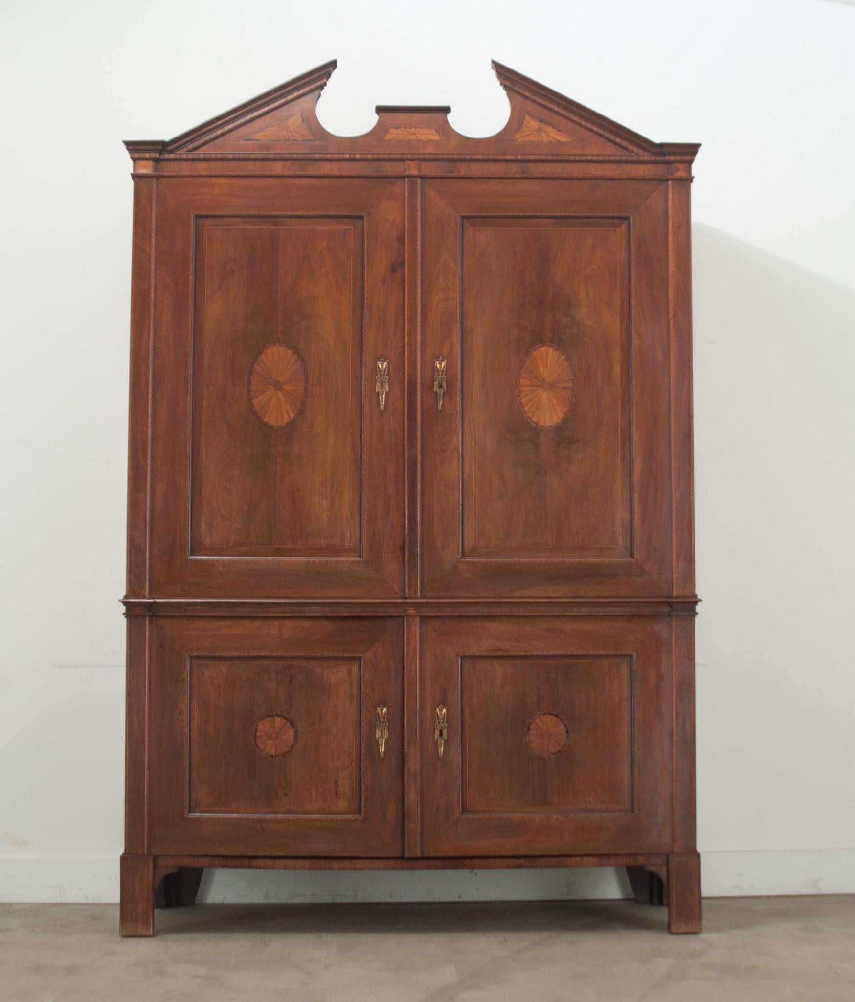 A mahogany Louis XVI period linen press made in the Netherlands. The top of this case piece has a broken pediment design over large bookmatched and paneled doors that open to reveal three fixed shelves, one at 9 ½” deep and two at 20 ½” deep, and 3