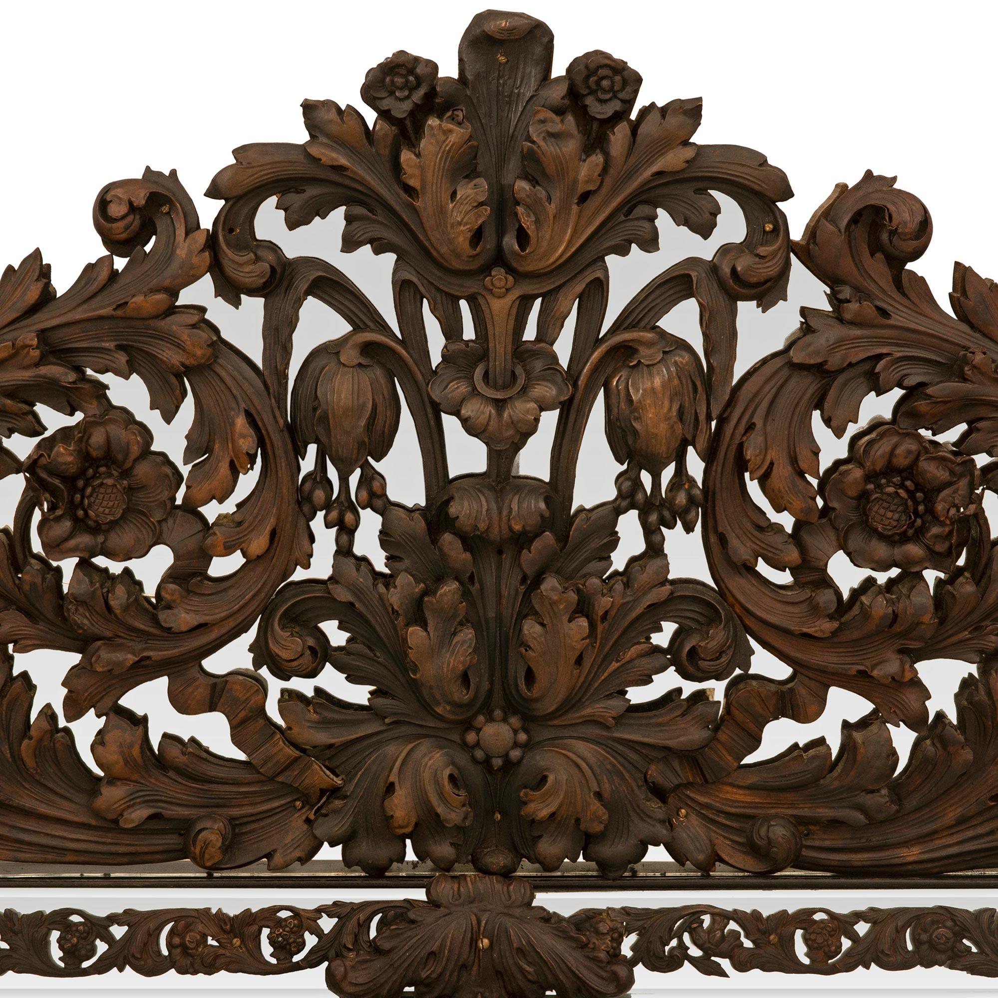 Miroir en métal pressé patiné de grande taille et de style baroque hollandais du XIXe siècle. Le miroir central biseauté d'origine est entouré d'un bandeau décoré de feuillages et de réserves dans les angles et à mi-hauteur. Chaque réserve percée