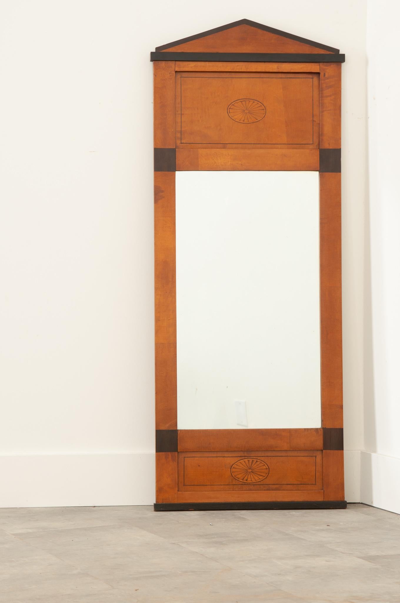 A fantastic tall and narrow satinwood Biedermeier style trumeau from 19th century Netherlands. The smart mirror has a clean, linear design with ebonized accents that contrast the satinwood frame marvelously. Two oval inlaid fan motifs embellish the