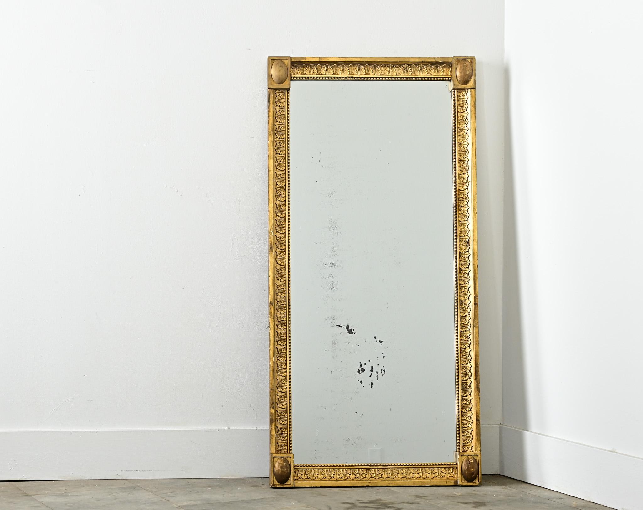A unique if not rare 19th century Dutch giltwood mirror that incorporates foliate decoration and Neoclassical carvings to animate the narrow, rectangular form. The molding displays a linear pattern of overlapping leaves, marked at the corners by