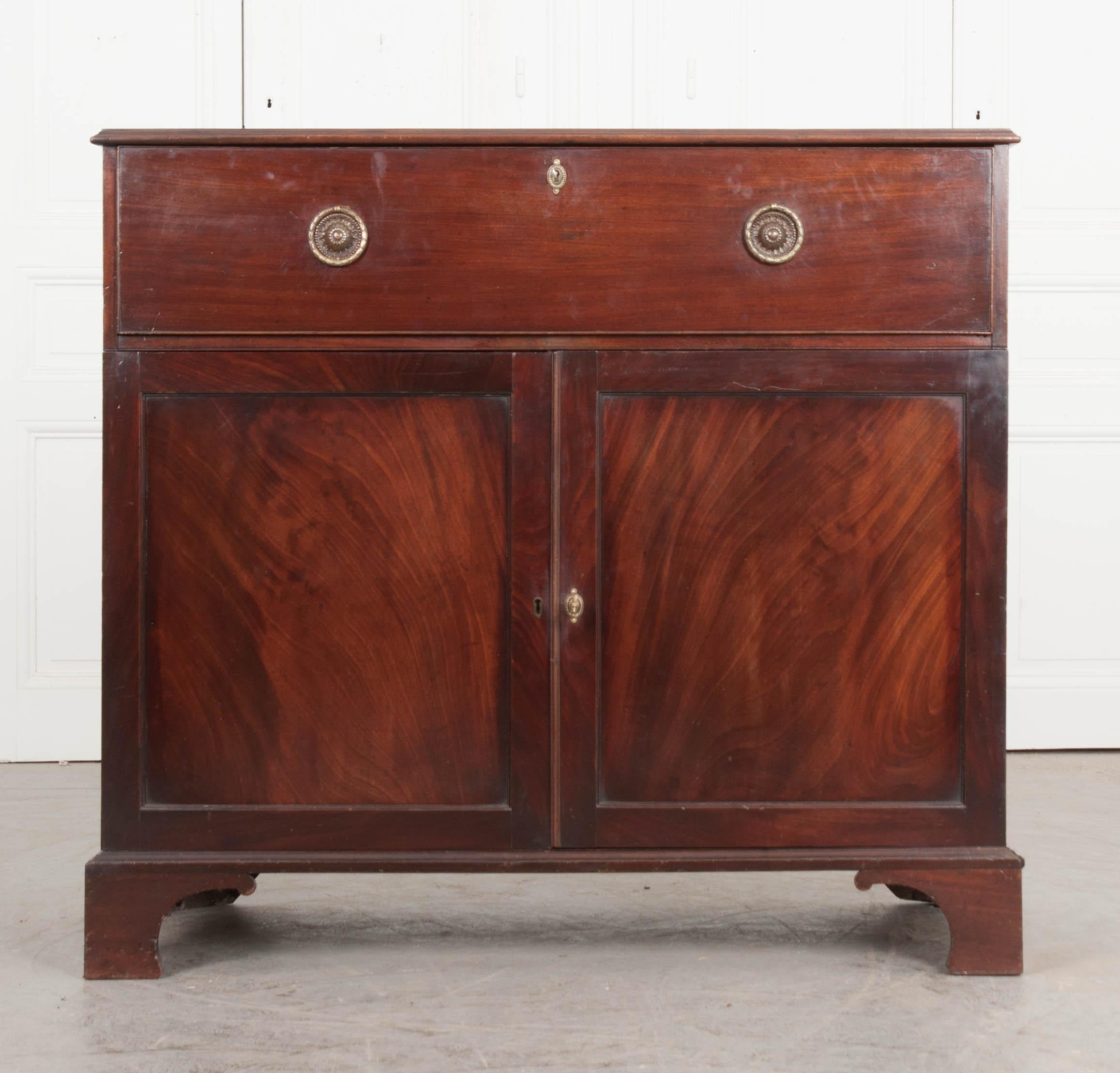 This 19th century flame mahogany drop-front secretary/linen press, circa 1860s, is a Dutch interpretation of the Classic English Georgian style. It features a drop-front writing surface with a bank of ten cubbies over a central drawer with brass