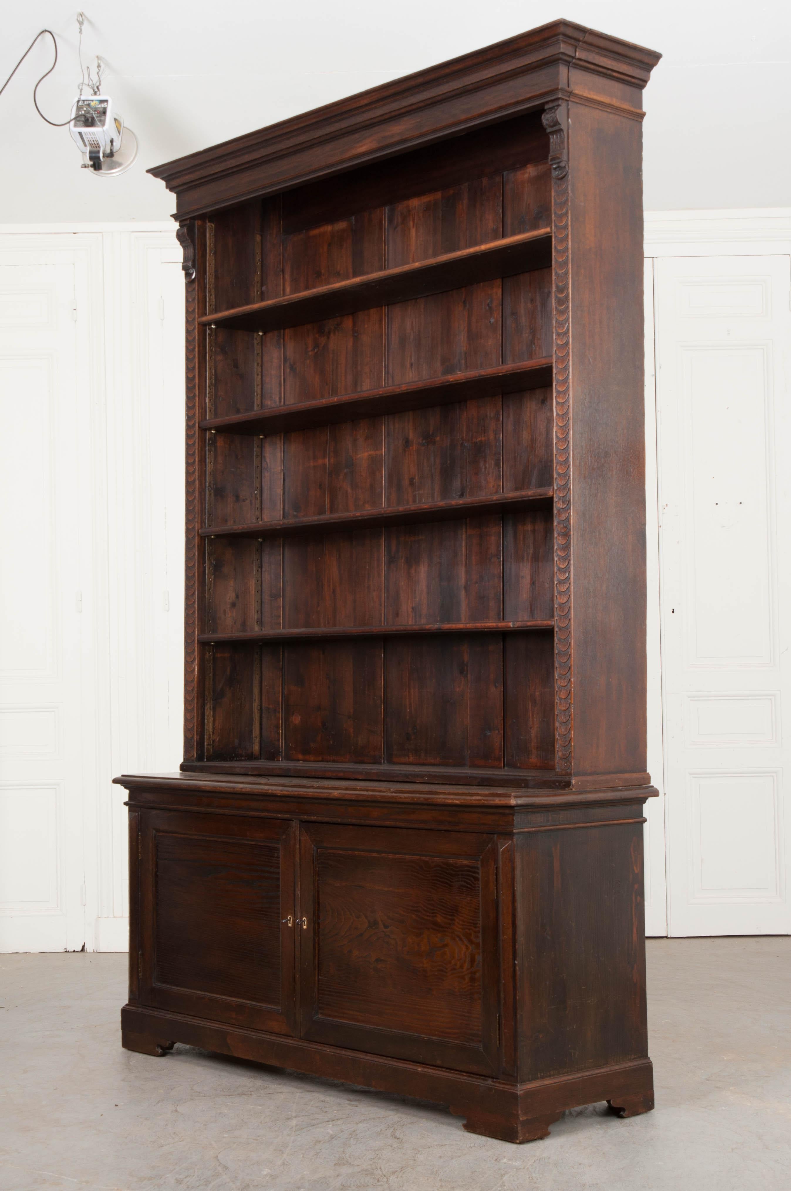 This impressive and large oak bookcase is from the Netherlands, circa 1860s, and breaks down into two pieces. The cornice’s front is hinged for ease of storing larger pieces and is likely a later addition. It rests above four adjustable shelves and