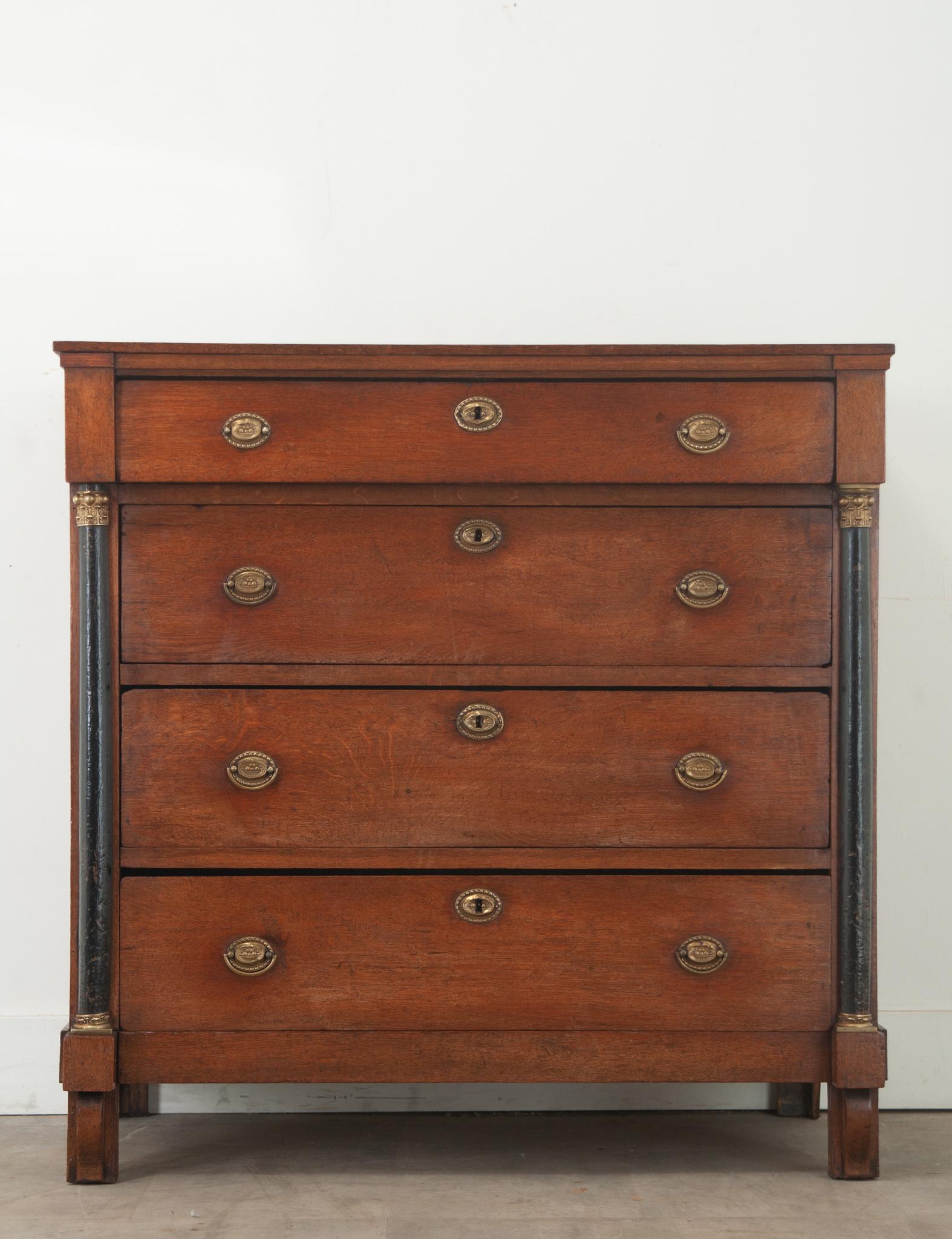 A classic Dutch Empire chest made of oak during the 1800’s. The top drawer protrudes forward over three drawers flaked with ebonized columns featuring brass capitals at the top and bases. All the drawers have brass escutcheon plates and ring pulls,