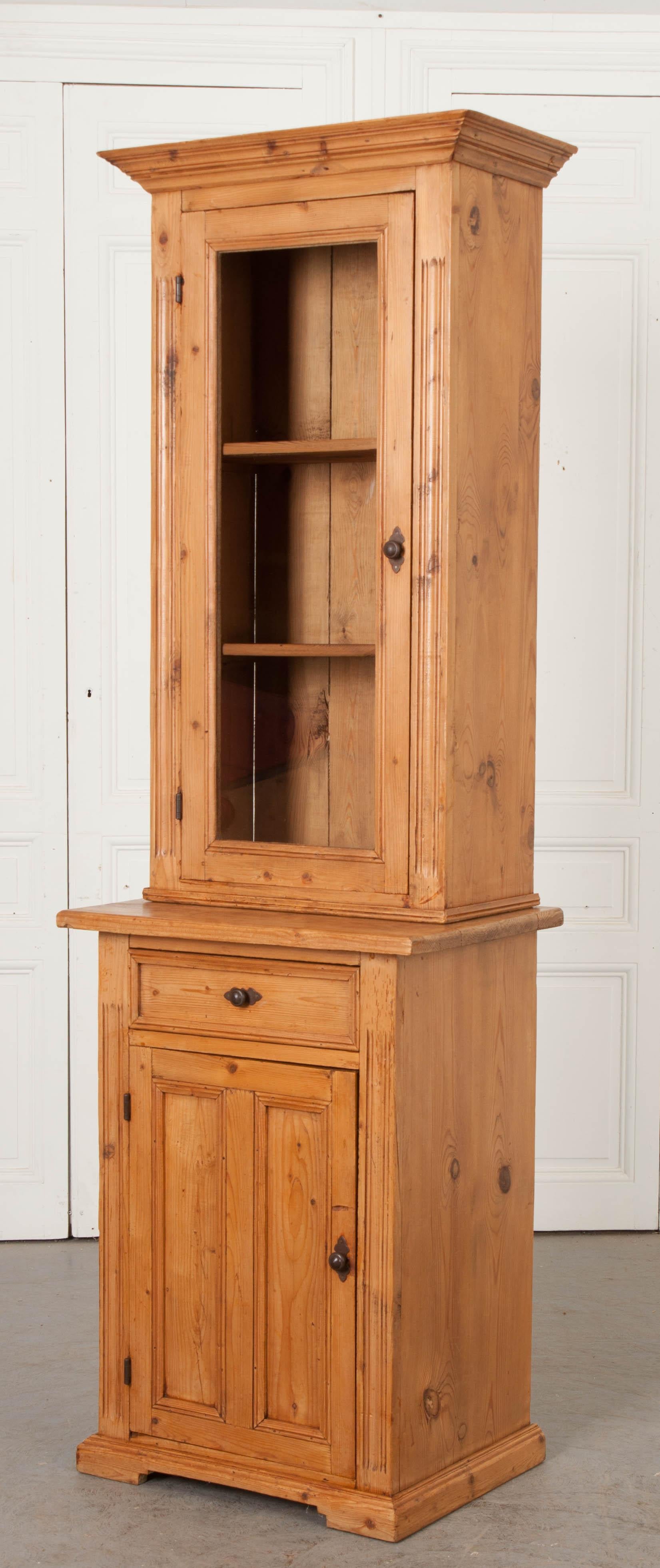 This charming narrow carved pine cabinet, circa 1880s, is from the Netherlands and features a well-carved cornice over an upper case having carved shoulders and a glazed and beaded door through which a pair of fixed shelves can be seen. The base has