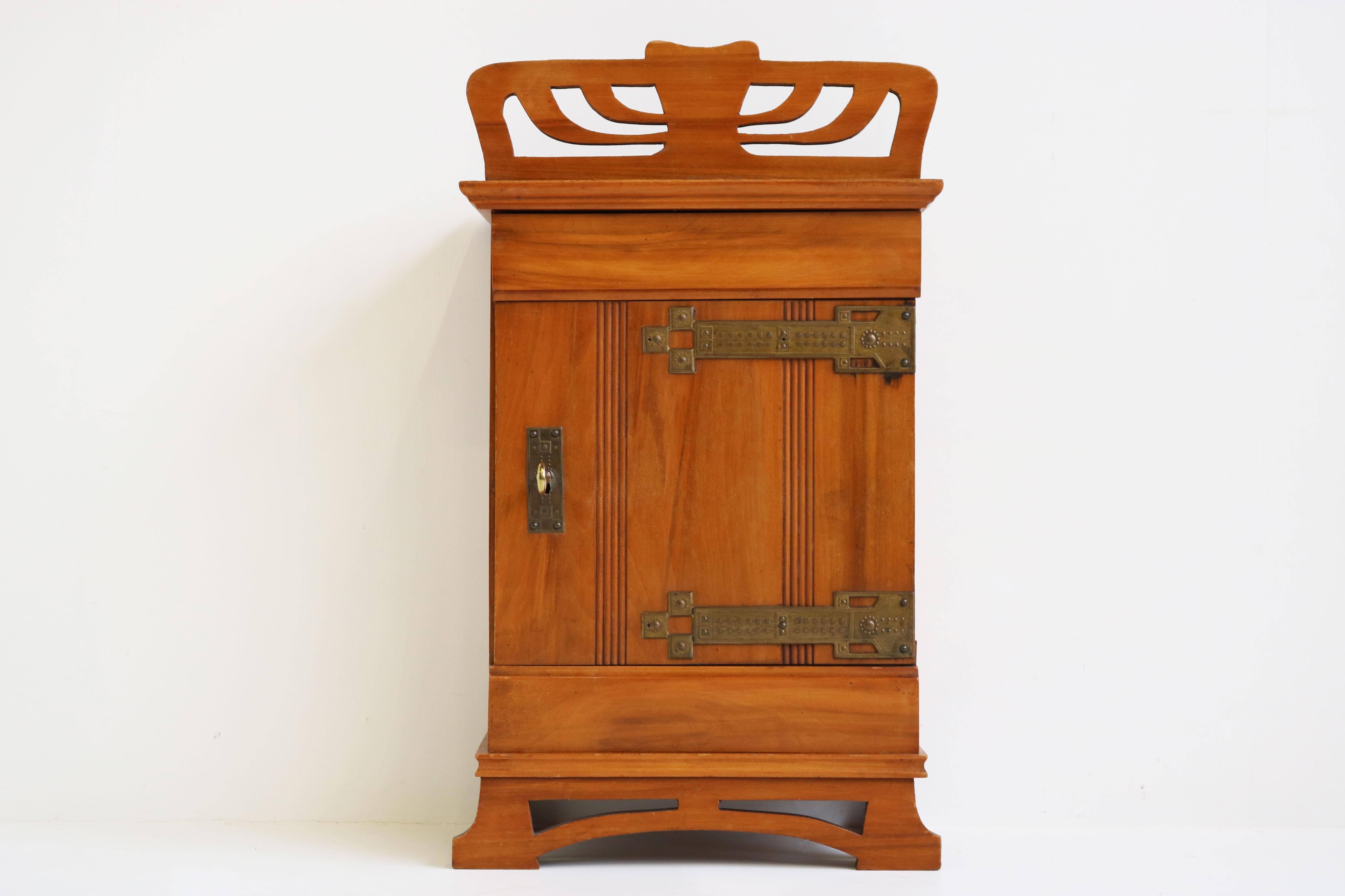 Gorgeous Dutch antique Art Nouveau wall cabinet from the 1910s. 
Gorgeous Art nouveau lines in solid wood with high quality brass decorations. (these could be considered Arts & crafts design style) 
The wall cabinet comes with a working lock and