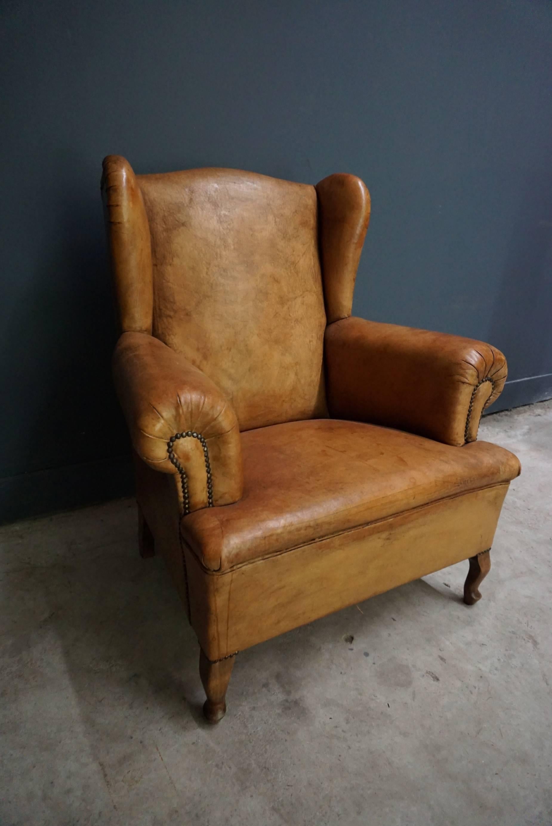 This club chair is upholstered with cognac-colored leather and features metal pins and wooden legs.