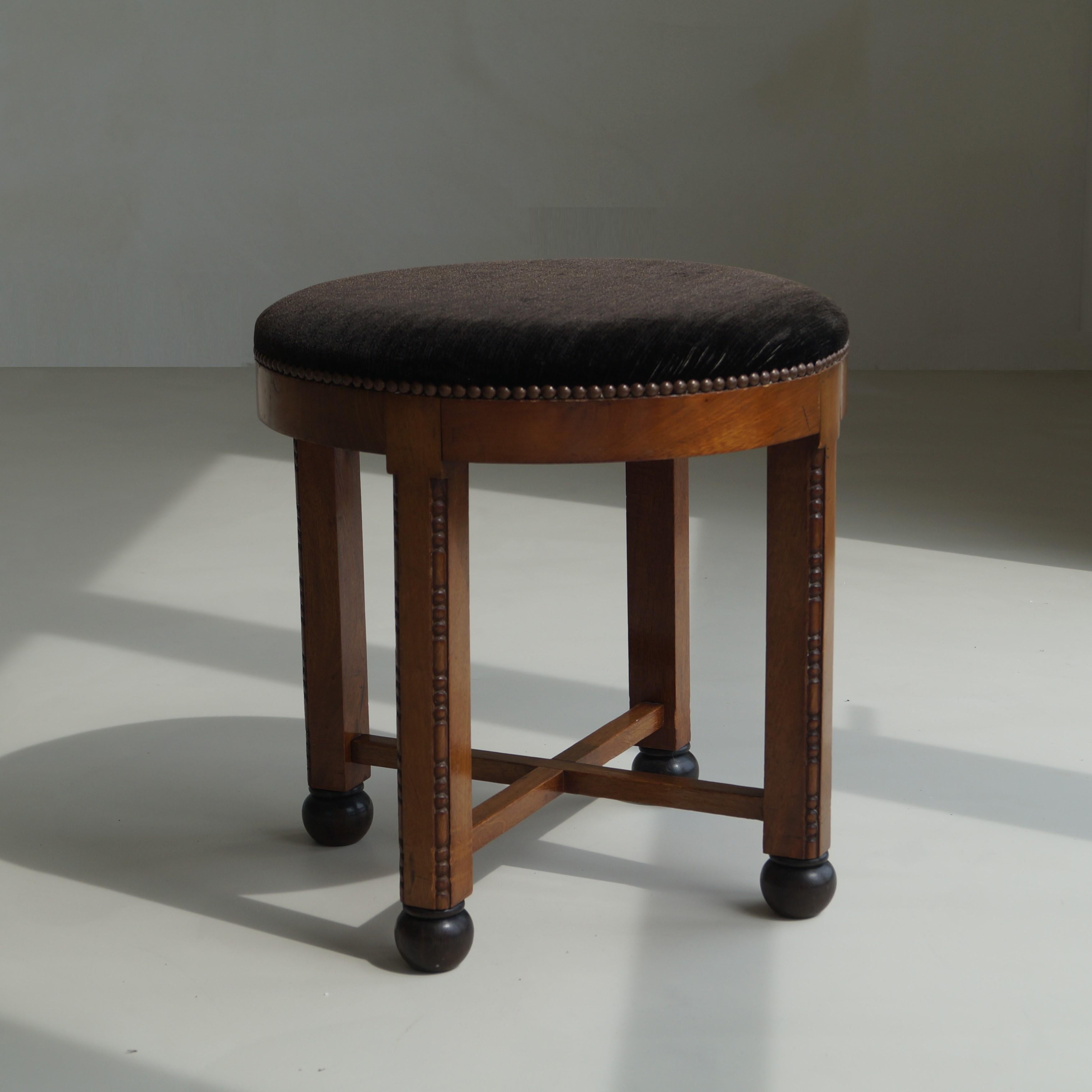 A very decorative original 1930s Amsterdam School stool in walnut with a vintage velvet like upholstery in a dark brown almost black colour. 
The piece has an unusual design because of the rather large seat, which has the same width as the height of